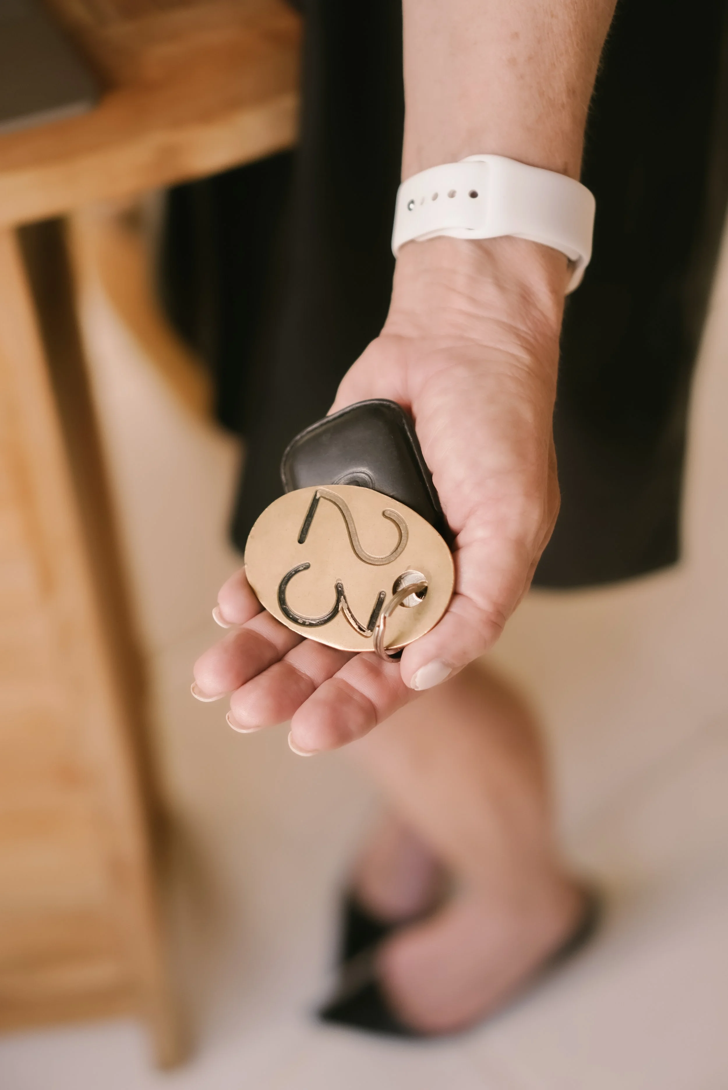 A person holding a black key fob with a leather keychain that has a large beige shape with black squiggly lines. The person is wearing a white wristwatch or fitness tracker.