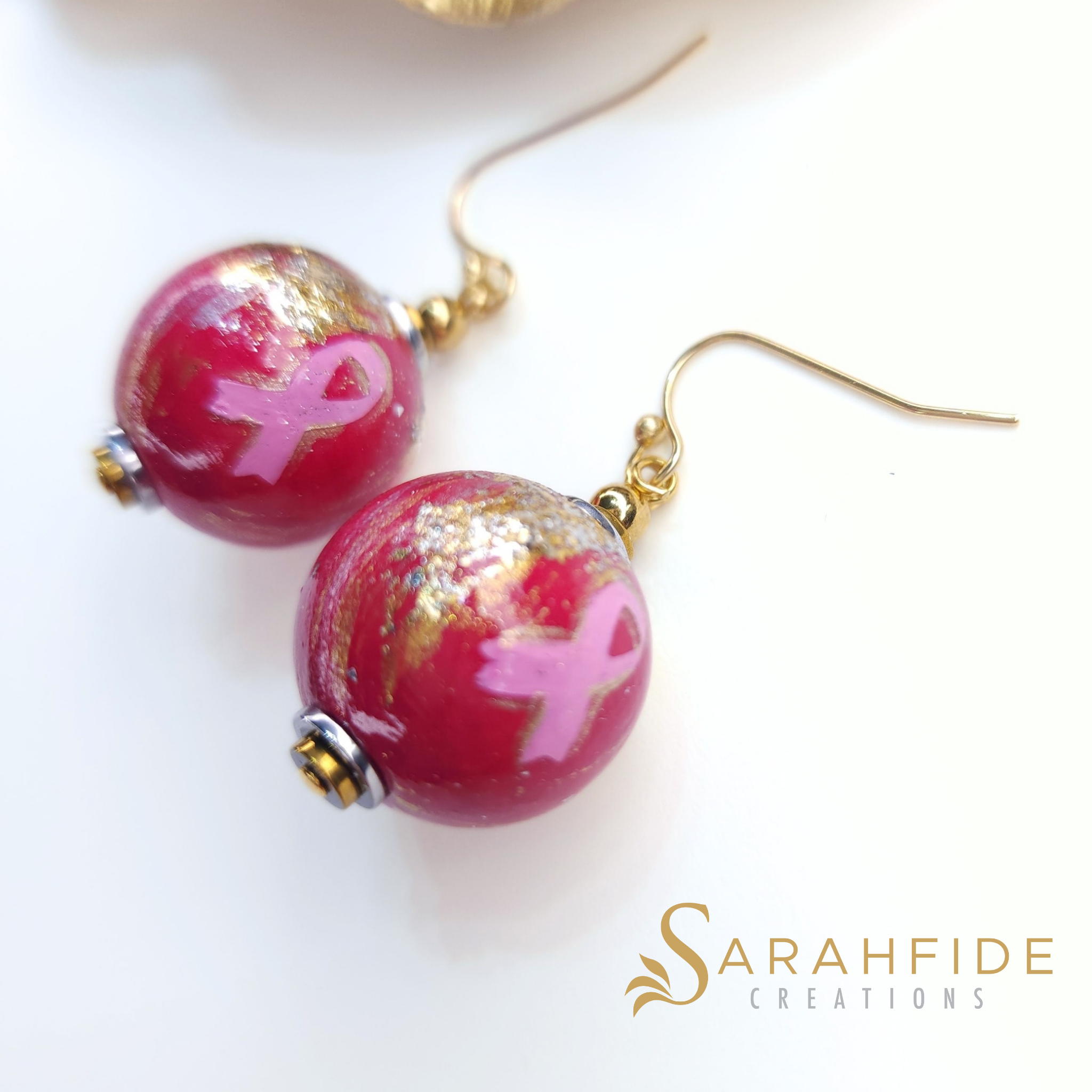 Close up of Breast Cancer Awareness earrings, deep pink beads with gold details and pink ribbons