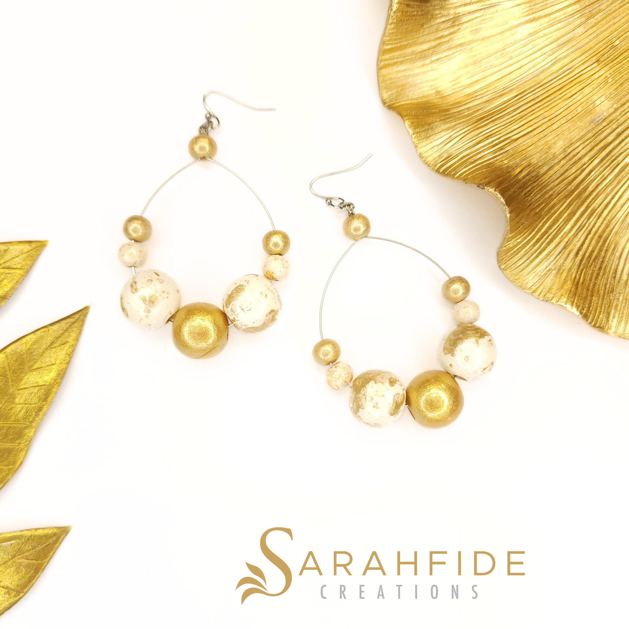 Pair of Gold Lux Large Round Drop Earrings laid flat with gold leaves