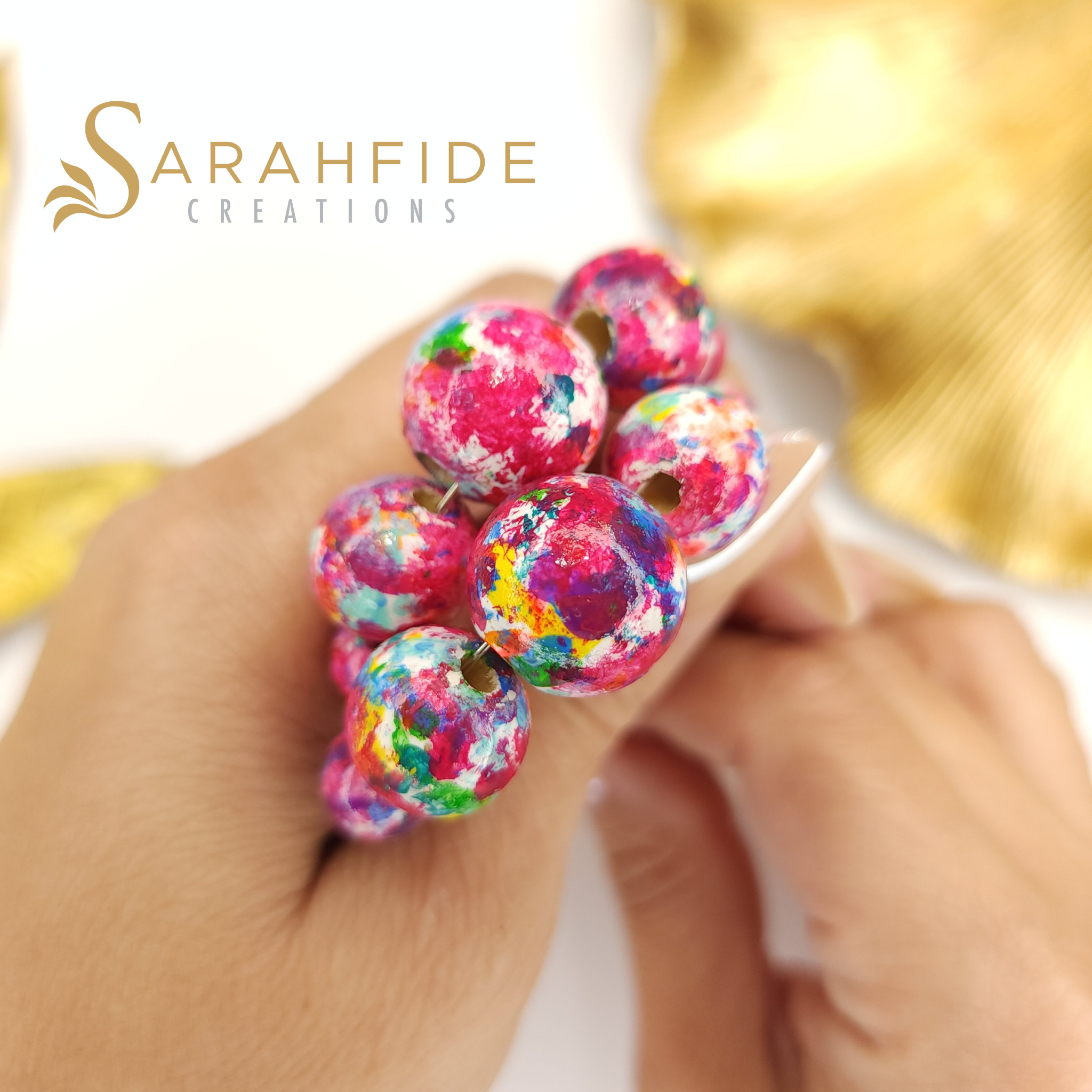 Close-up of Garden Goddess beads in pink, teal, yellow and green held in a hand