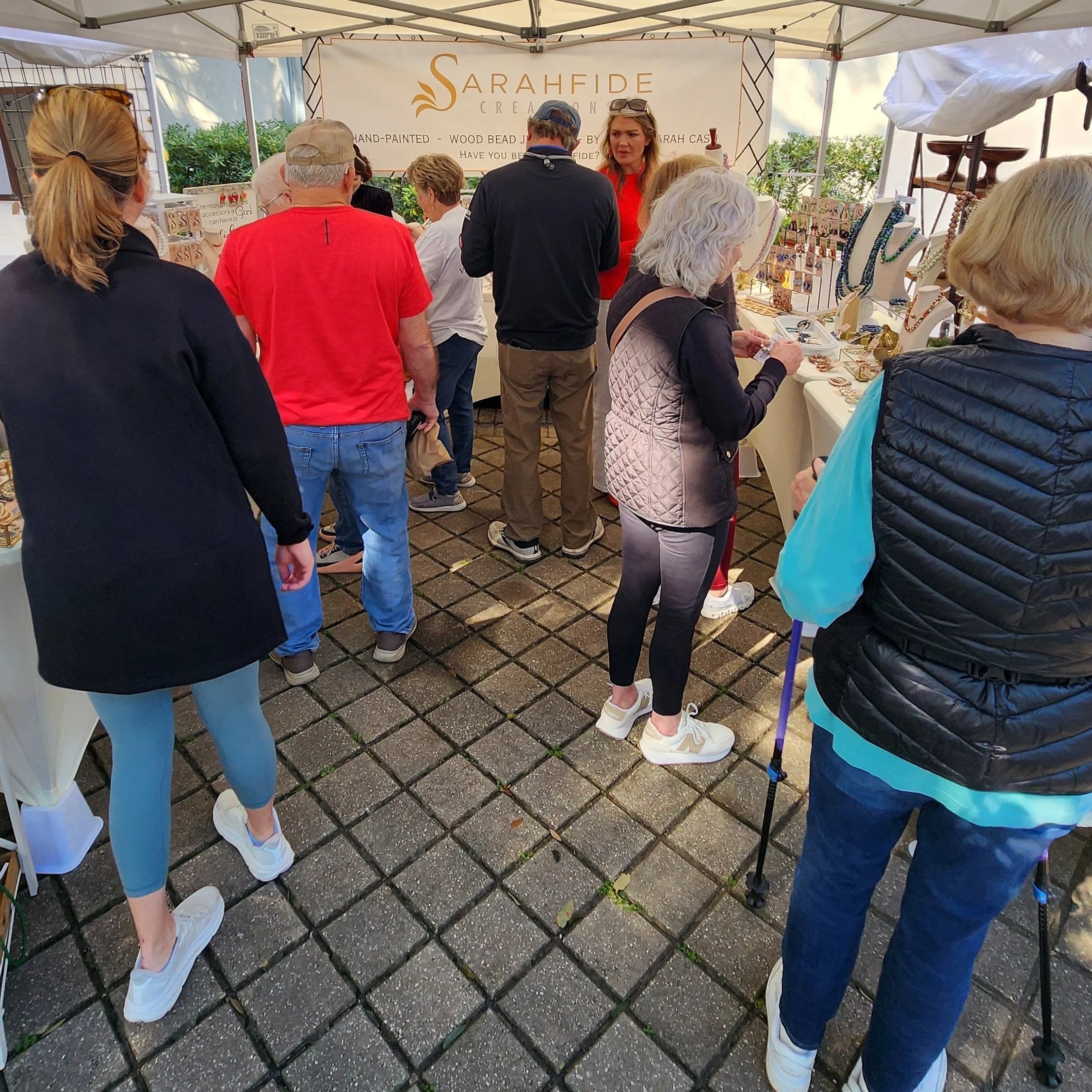 Shoppers browsing hand-painted wood bead earrings and jewelry at Sarahfide's booth at Crafts in the Village, St. Simons Island, Georgia