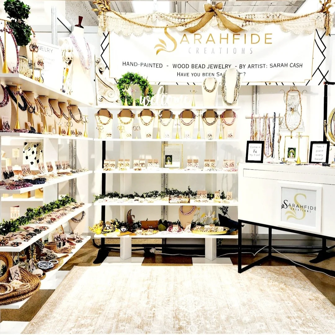 Sarahfide market booth with white shelves of hand-painted wood bead necklaces, bracelets and earrings