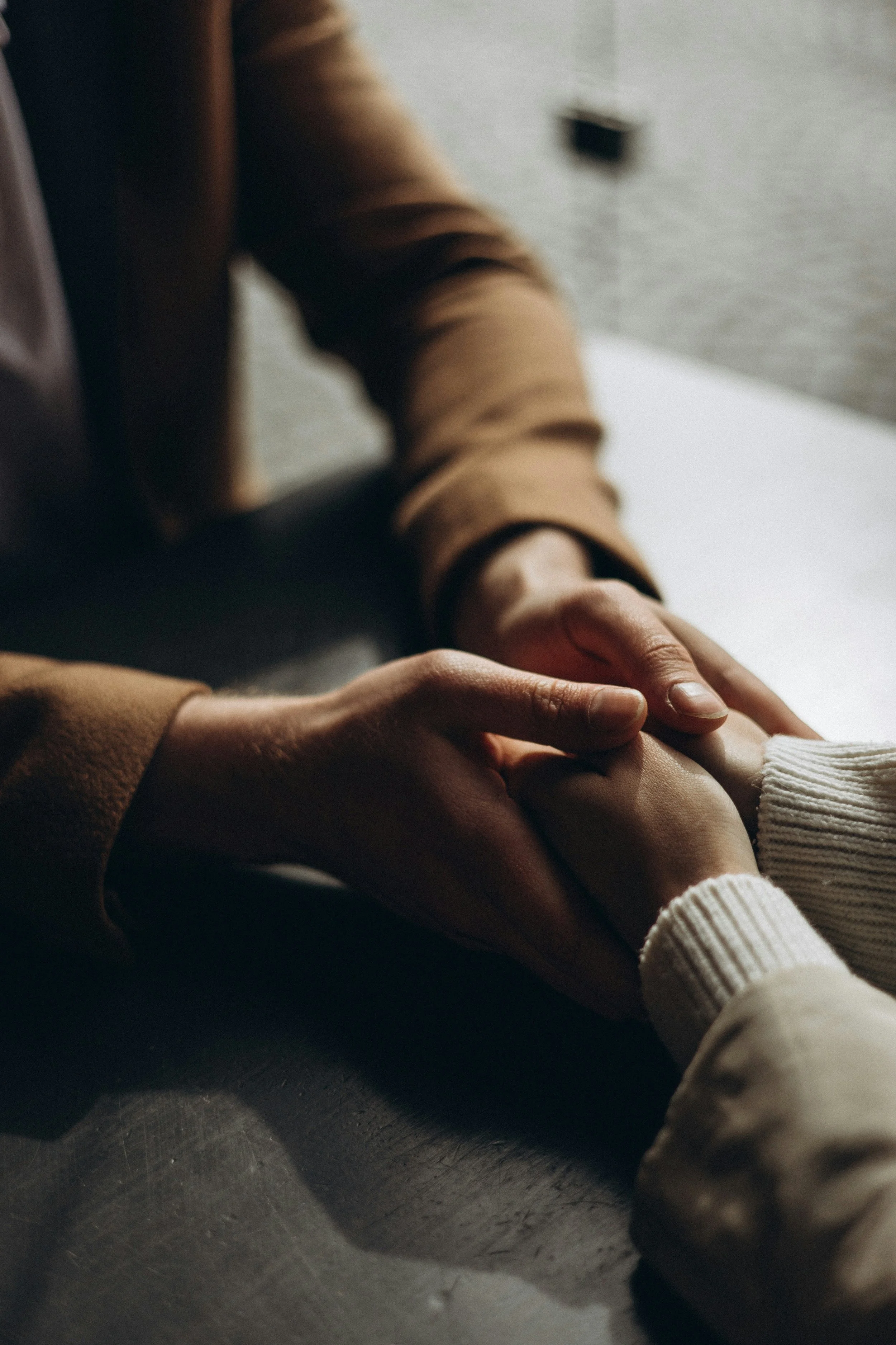 a close up on two people holding hands, one person is holding the others hands in theirs
