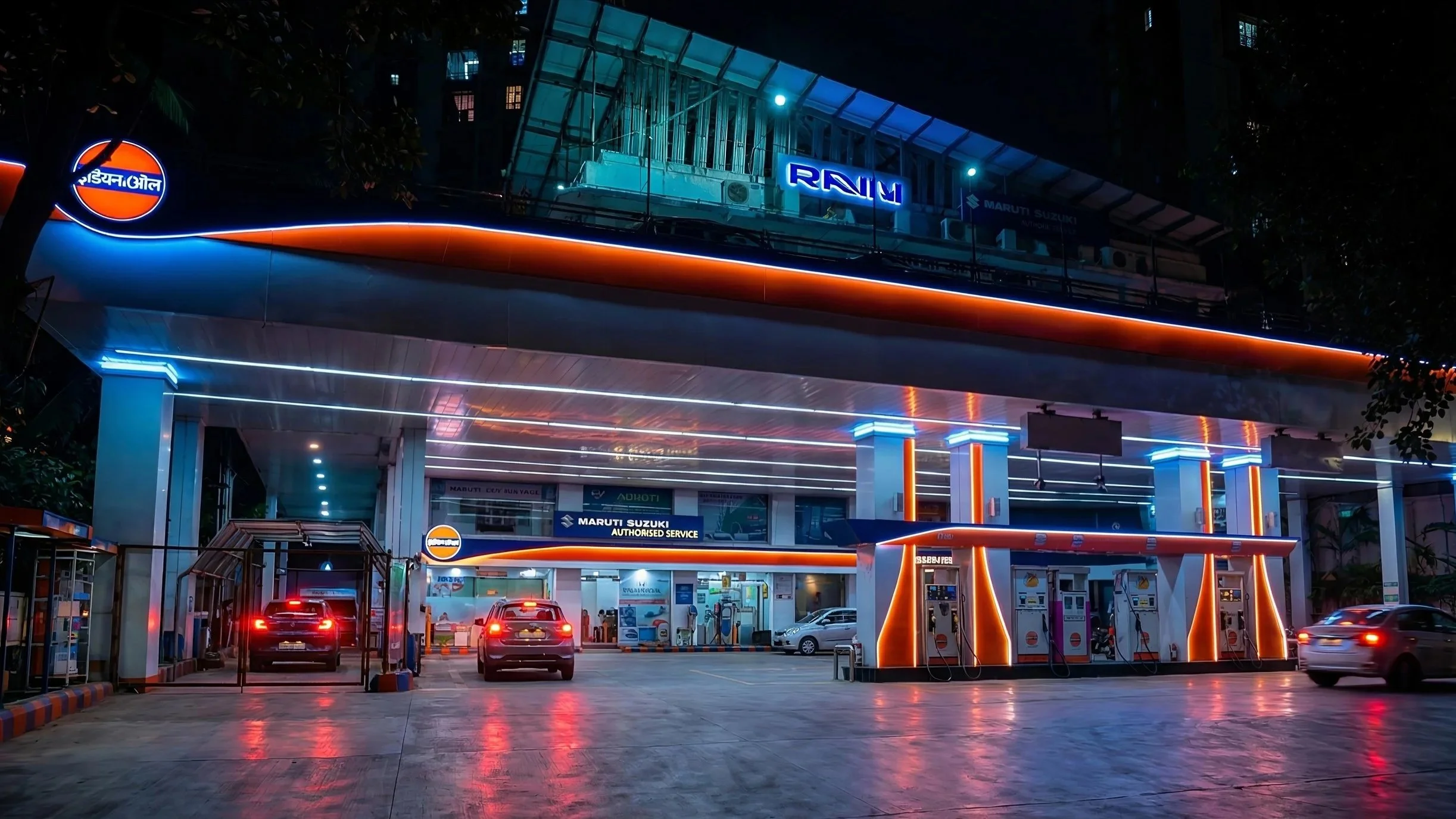 A busy petrol station with multiple cars parked and fueling, surrounded by trees, with a multi-story building in the background, and the ground appears wet from recent rain.