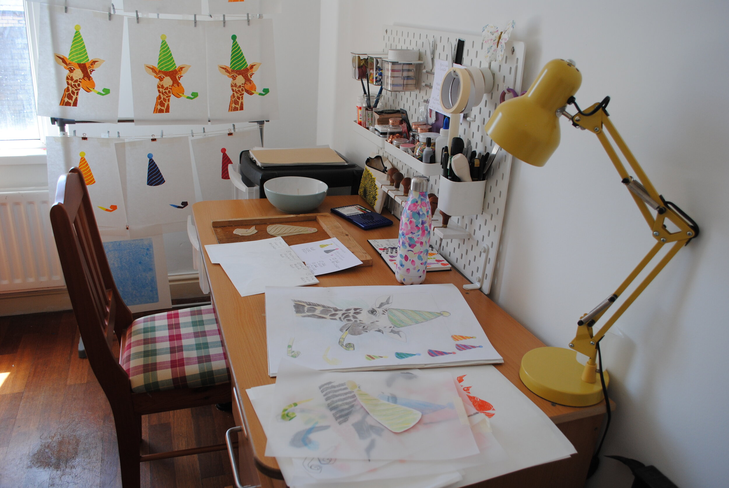 Home Printmaking Studio. Ikea Peg Board. Sketchbook open. Reduction linocut print drying on the rack.JPG
