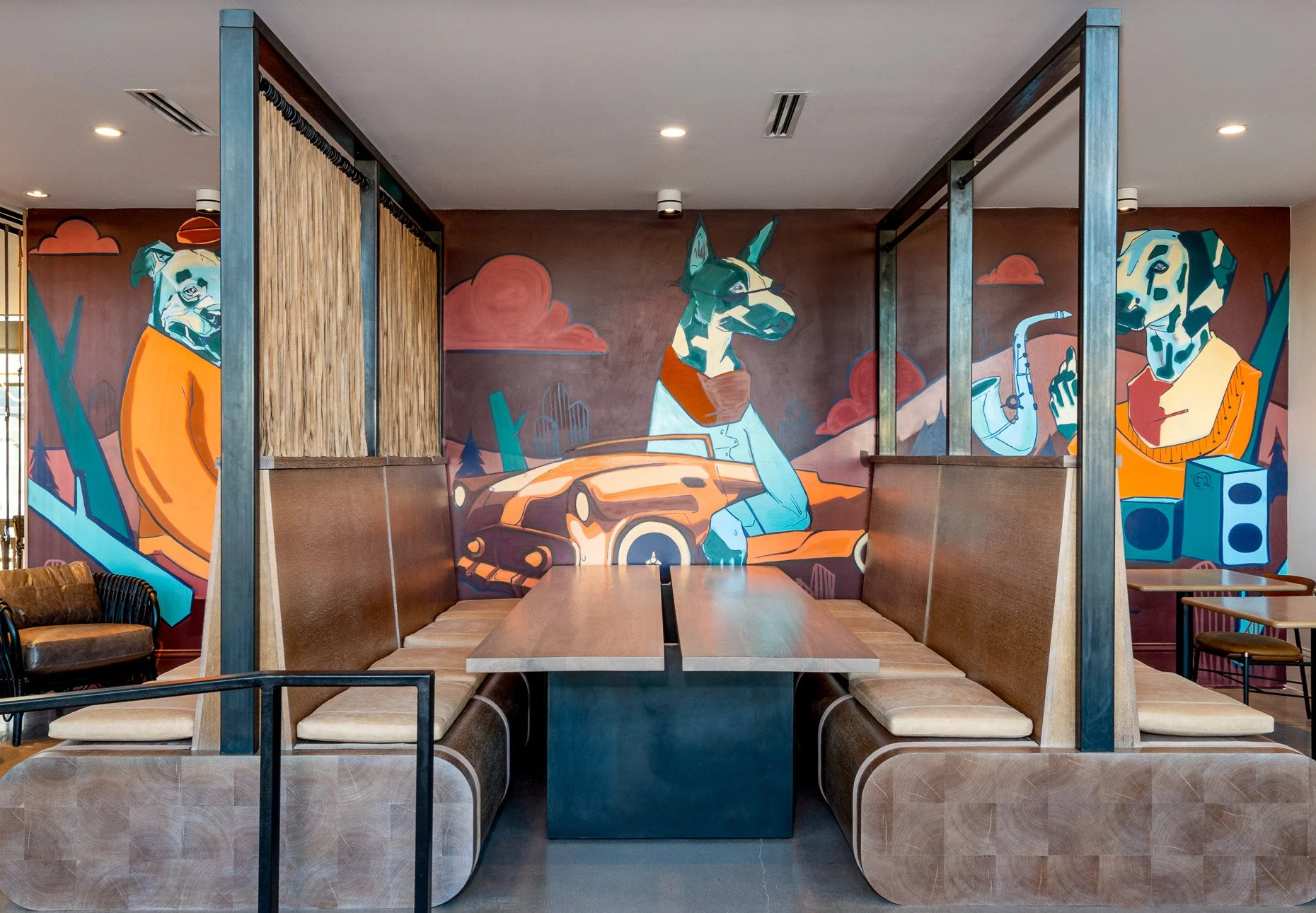Booth seating in a modern Denver apartment complex  with warm leather benches, wood table, and colorful dog-themed mural artwork creating a vibrant, contemporary interior design backdrop.