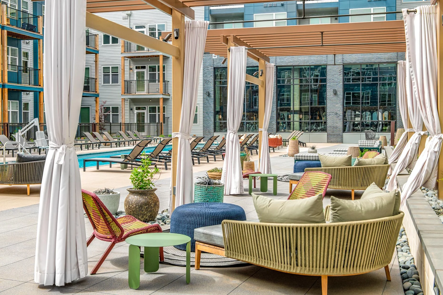Resort-style pool courtyard at AVA RiNo Apartments in Denver featuring cabana-style pergolas with white curtains, colorful lounge seating, and rows of sun loungers surrounding the swimming pool.