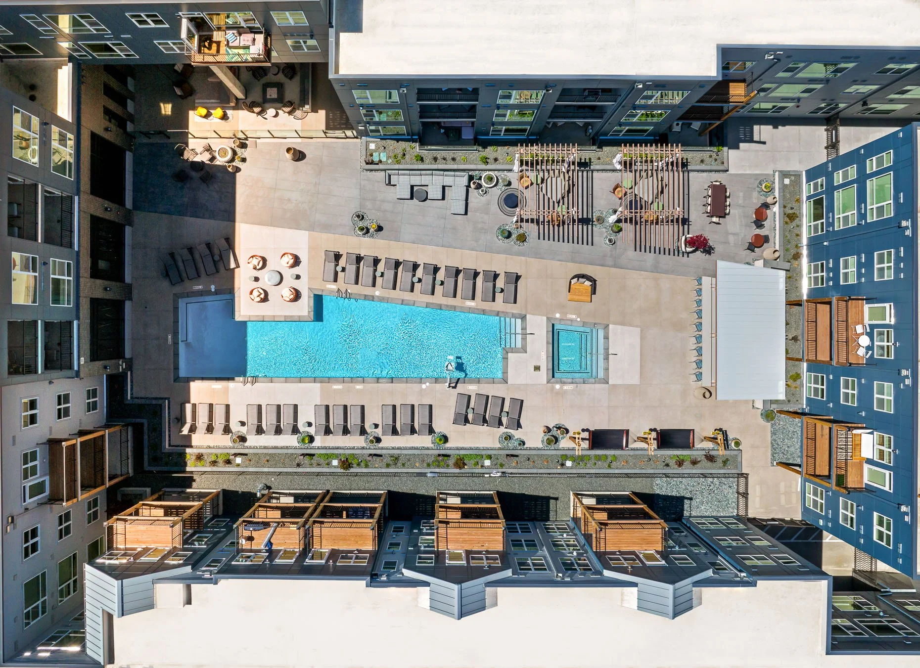 Straight-down drone view of AVA RiNo’s central courtyard showing a long rectangular pool, spa, lounge chairs, and outdoor amenity spaces framed by modern apartment buildings.