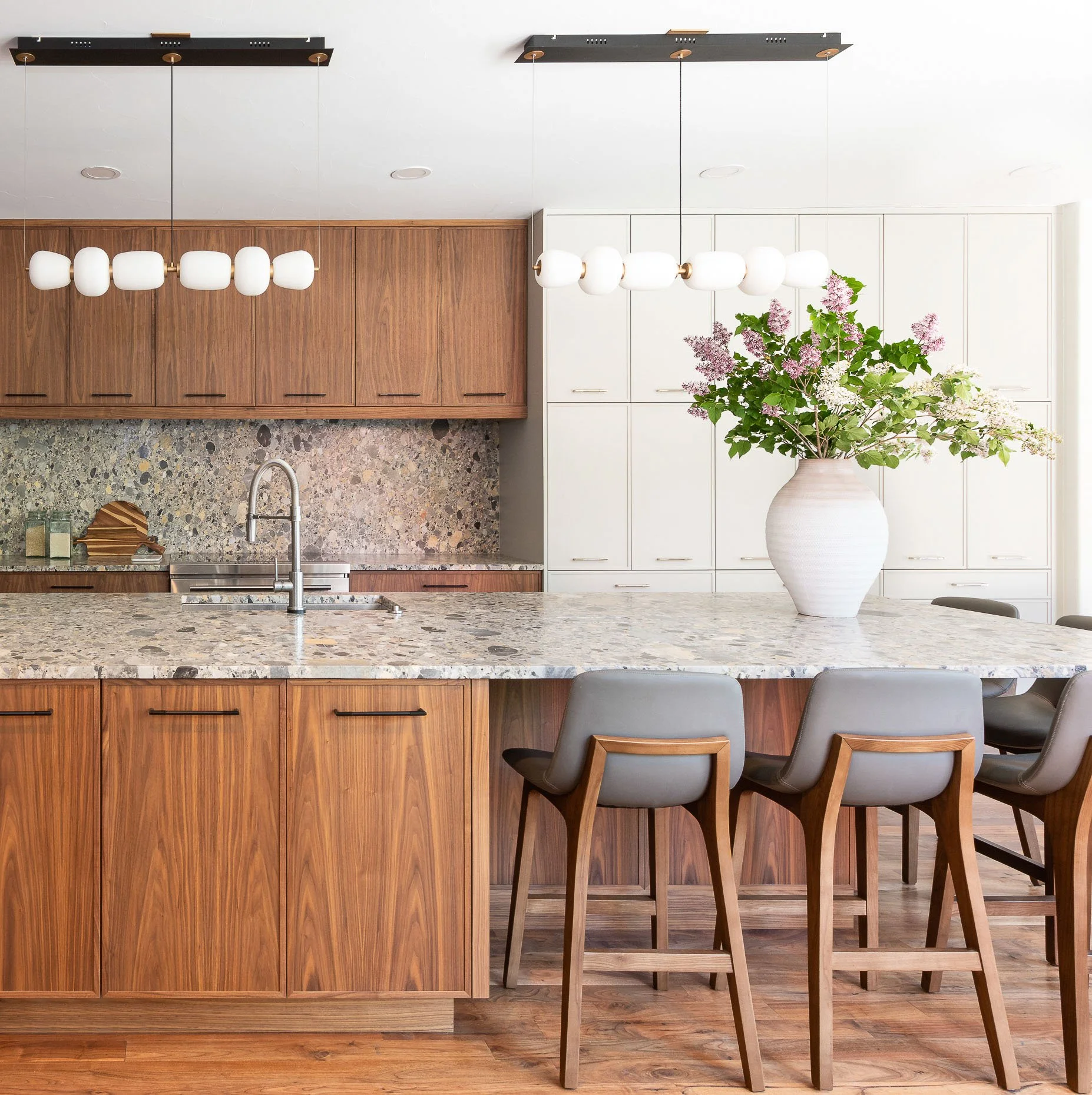 Elegant kitchen featuring a polished stone countertop, warm cabinetry, pebble-textured backsplash and modern pendant lighting for a sophisticated design.