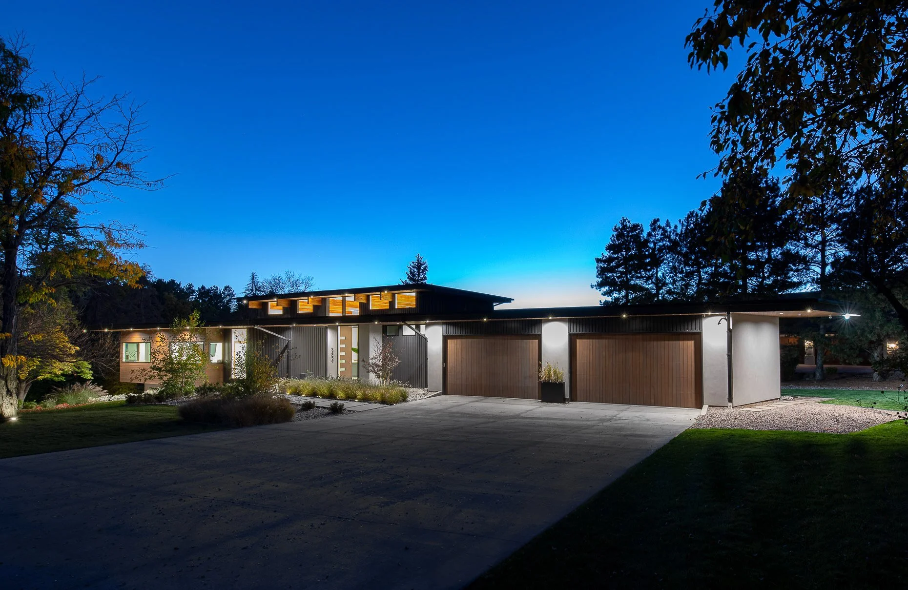Sleek contemporary home exterior, showcasing a sophisticated architectural design with a minimalist flat roof,  and expansive garage doors. Thoughtfully placed outdoor lighting enhances the stylish and cutting-edge aesthetic.
