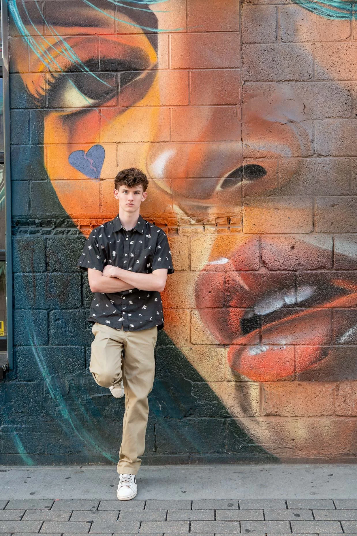 High School Senior with crossed arms leaning against a professional graffiti wall in RiNo Art District of Denver