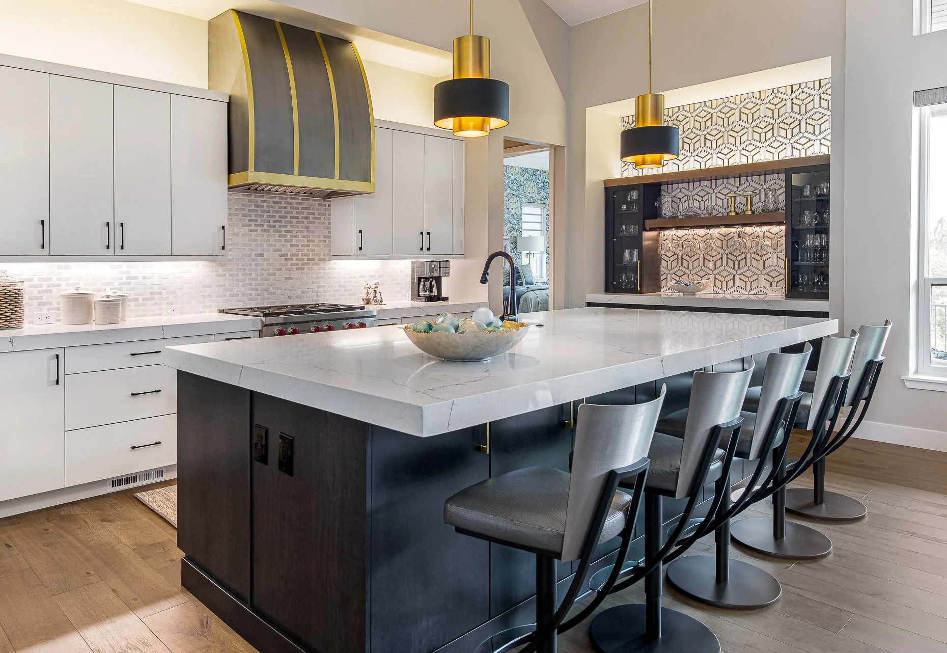 Modern kitchen with white cabinetry, black and gold range hood, marble island with bar stools, and decorative wall behind the bar area.