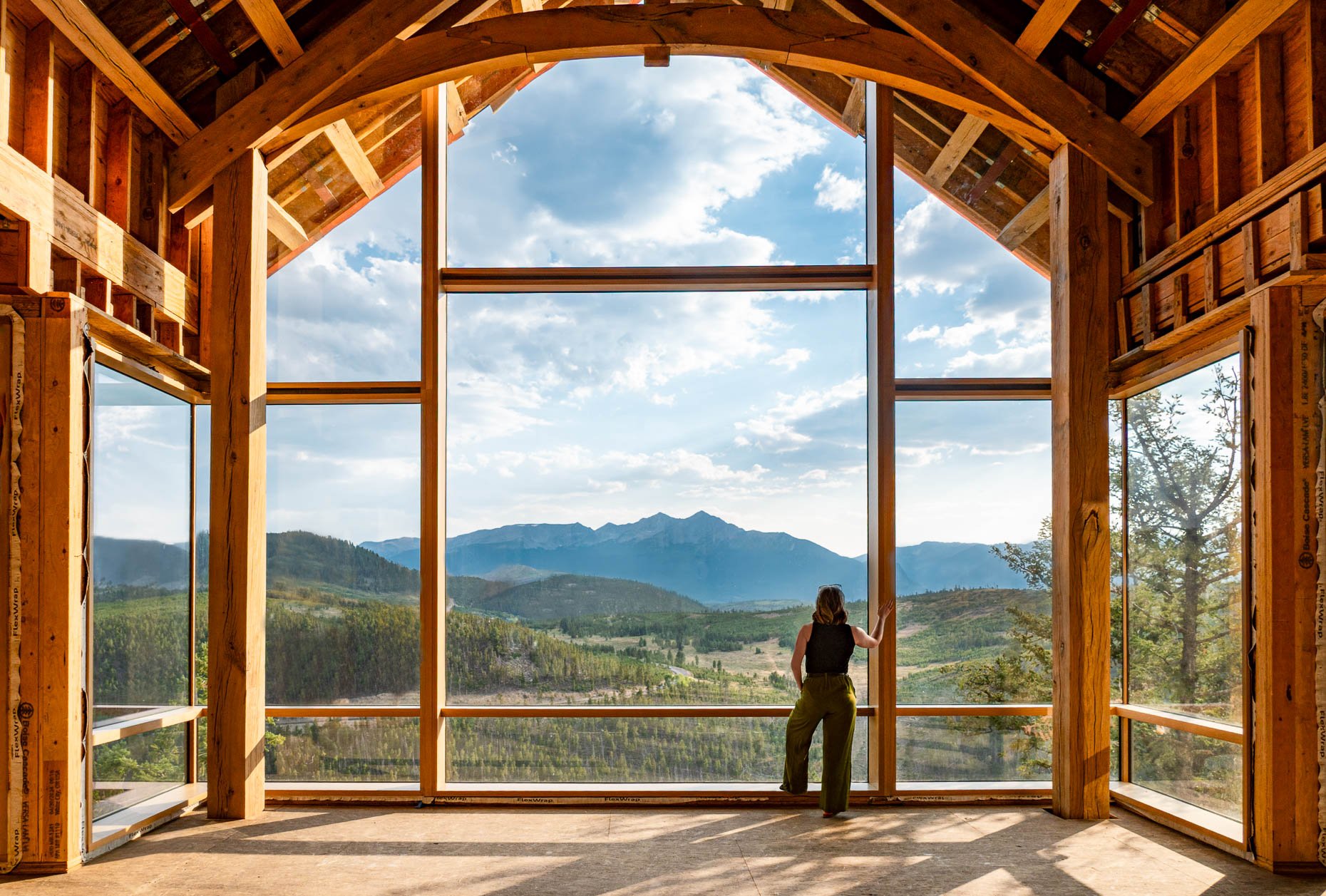 Photograph of a building project with a 3 story window overlooking river and mountain views. A woman stands looking out over the view
