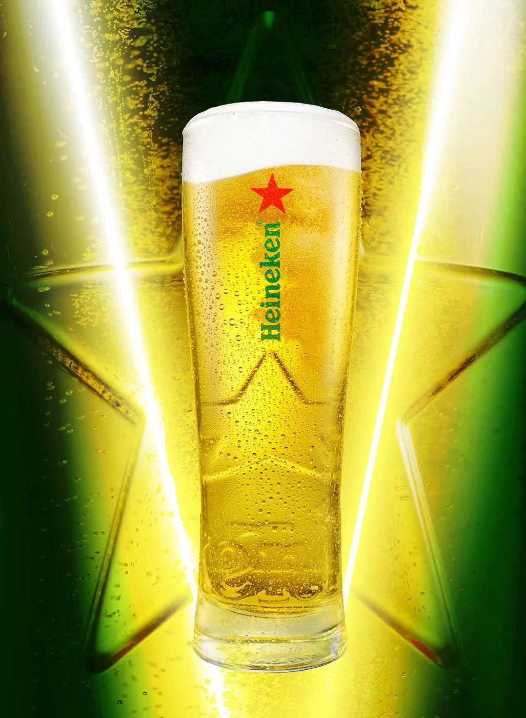 Studio photograph of a Heineken beer glass filled with golden lager and foam, backlit with a green star motif by NYC still life photographer Takamasa Ota.
