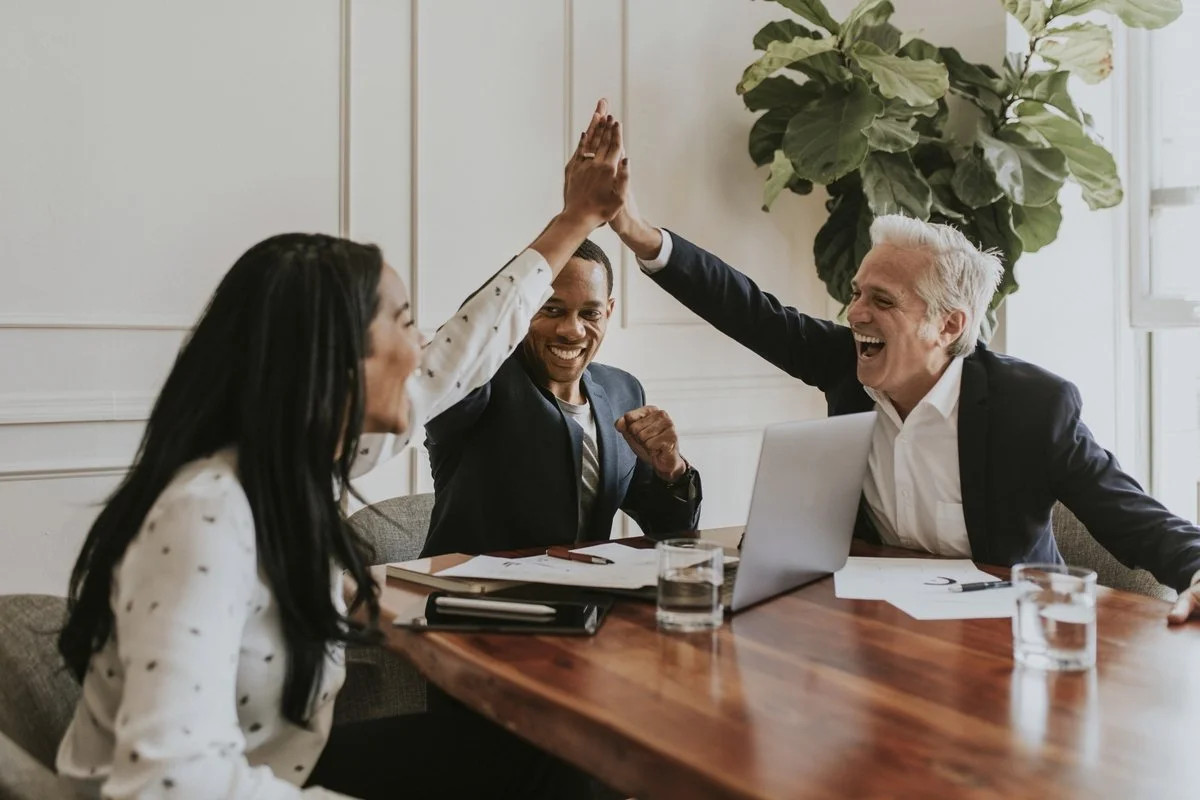 Three colleagues celebrating a successful project in a meeting room, giving high-fives and smiling.