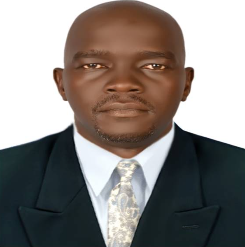 A man in a formal black suit, white shirt, and patterned tie, with a serious expression, against a plain white background.
