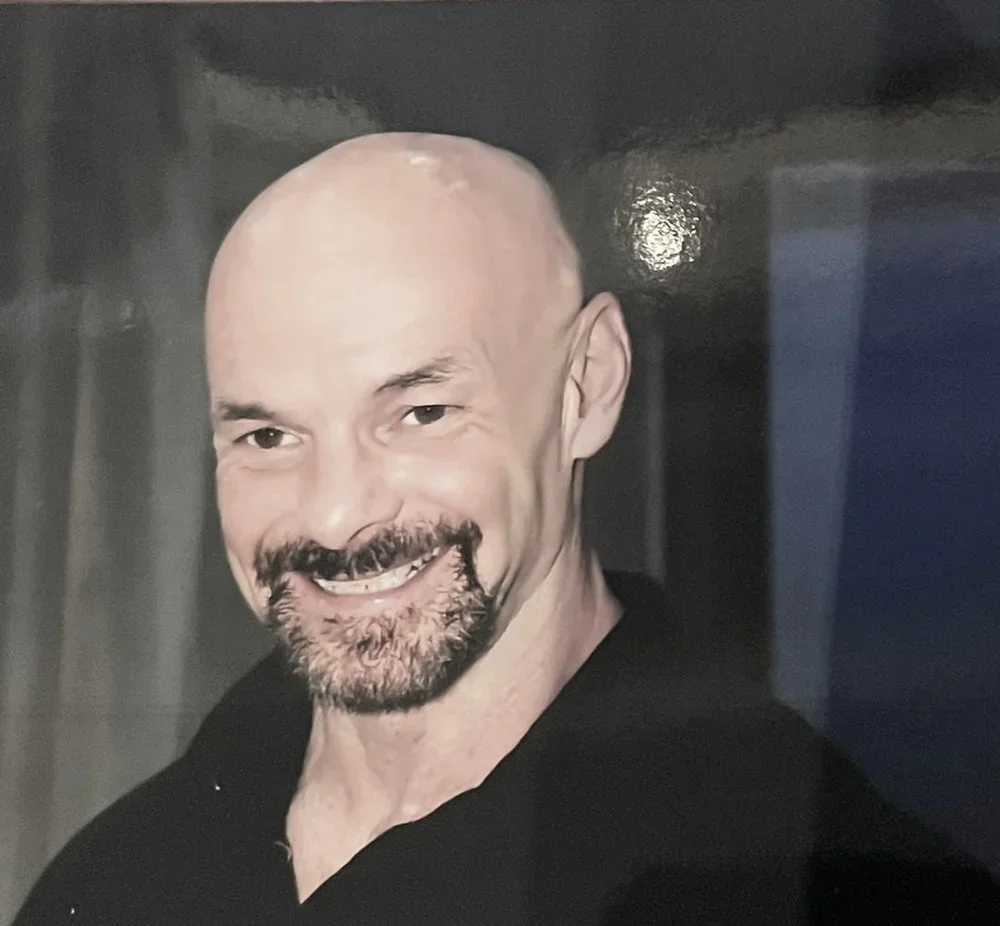 A smiling bald man with a beard and mustache wearing a black shirt.