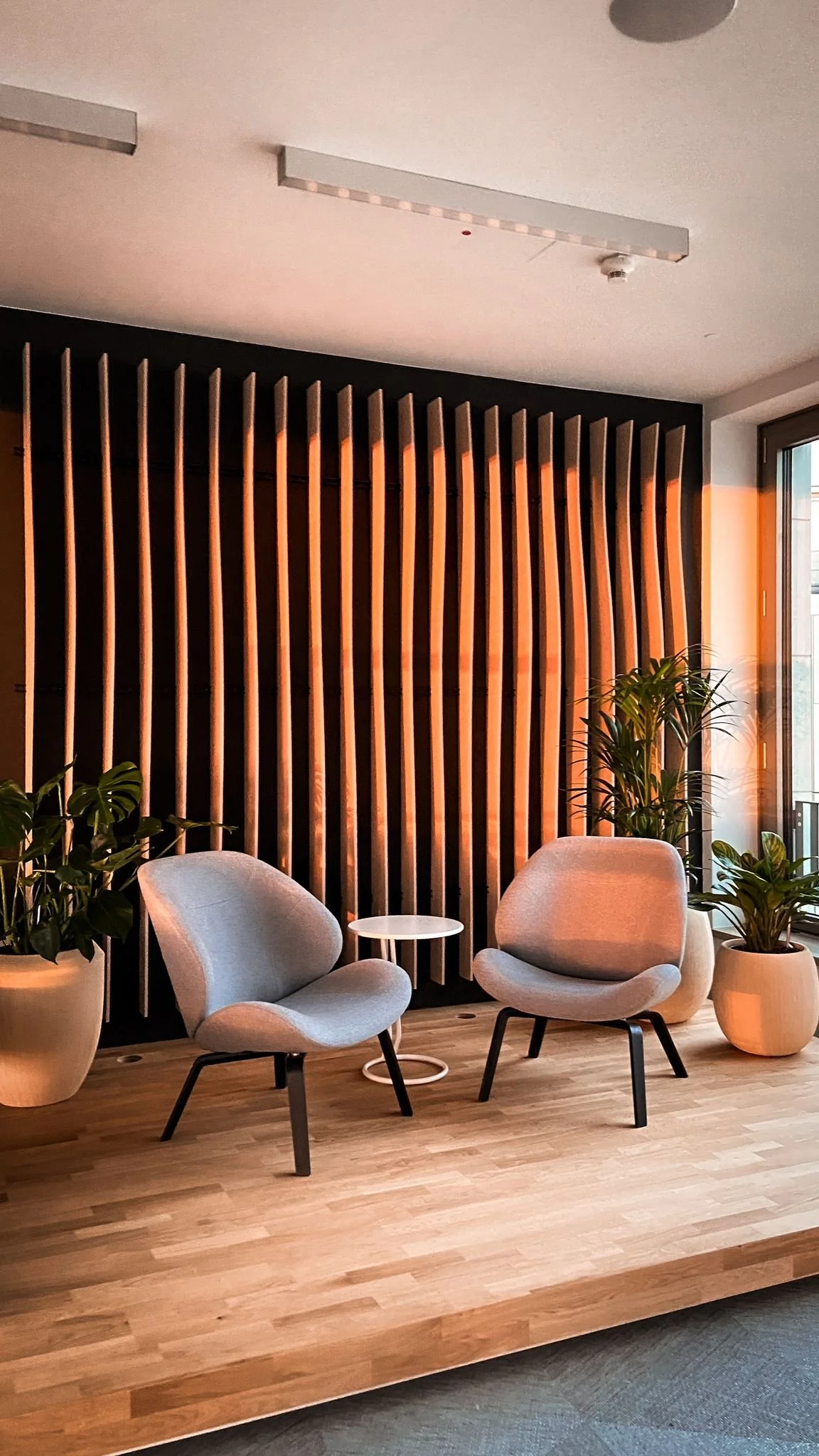 Dentsu Office: Raum mit zwei Stühlen und rundem Tisch in der Mitte dazwischen. Daneben Planzen. Wand hat Holzlamellen von oben bis unten. Themenbereich: Interiorgestaltung, Innenarchitektur, Placemaking.