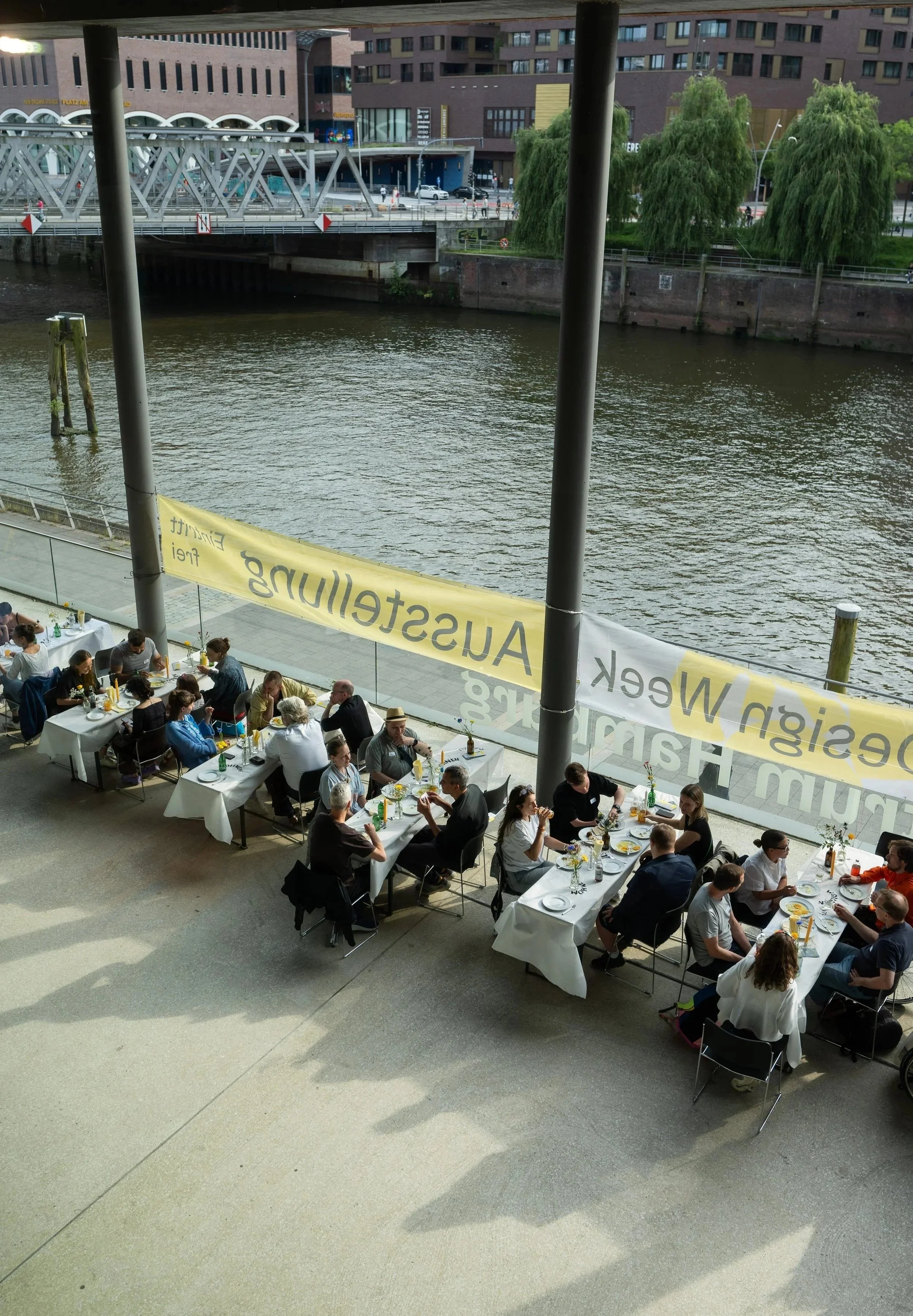 Menschen sitzen an Tischen im Restaurant am Wasser bei gutem Wetter.