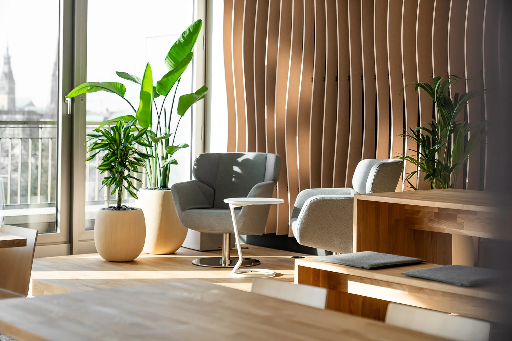 Dentsu Office: Blick in einen Raum mit Laminatfußboden. Am Ende stehen Pflanzen in Kübeln und ein Stuhl mit Tisch vor bodentiefen Fenstern. Themenbereich: Interiorgestaltung, Innenarchitektur, Placemaking.