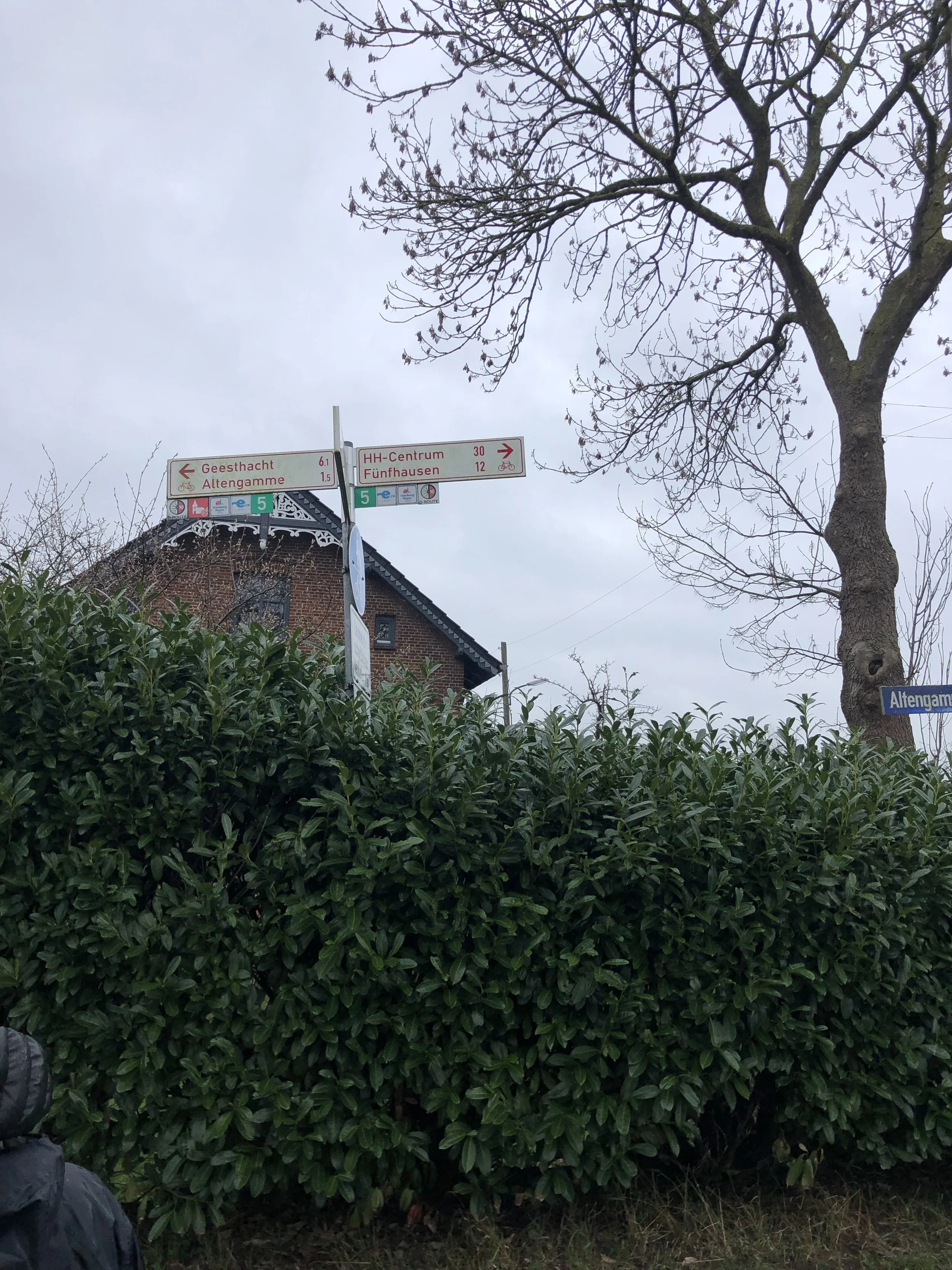 Foto aus den Vier- und Marschlanden. Im Vordergrund eine hohe Hecke und darüber Hinweisschilder mit Entfernungen, z.B. zum HH-Centrum.  Projekt Mobilitätskonzept Vier- und Marschlande von CITIES FOR FUTURE.