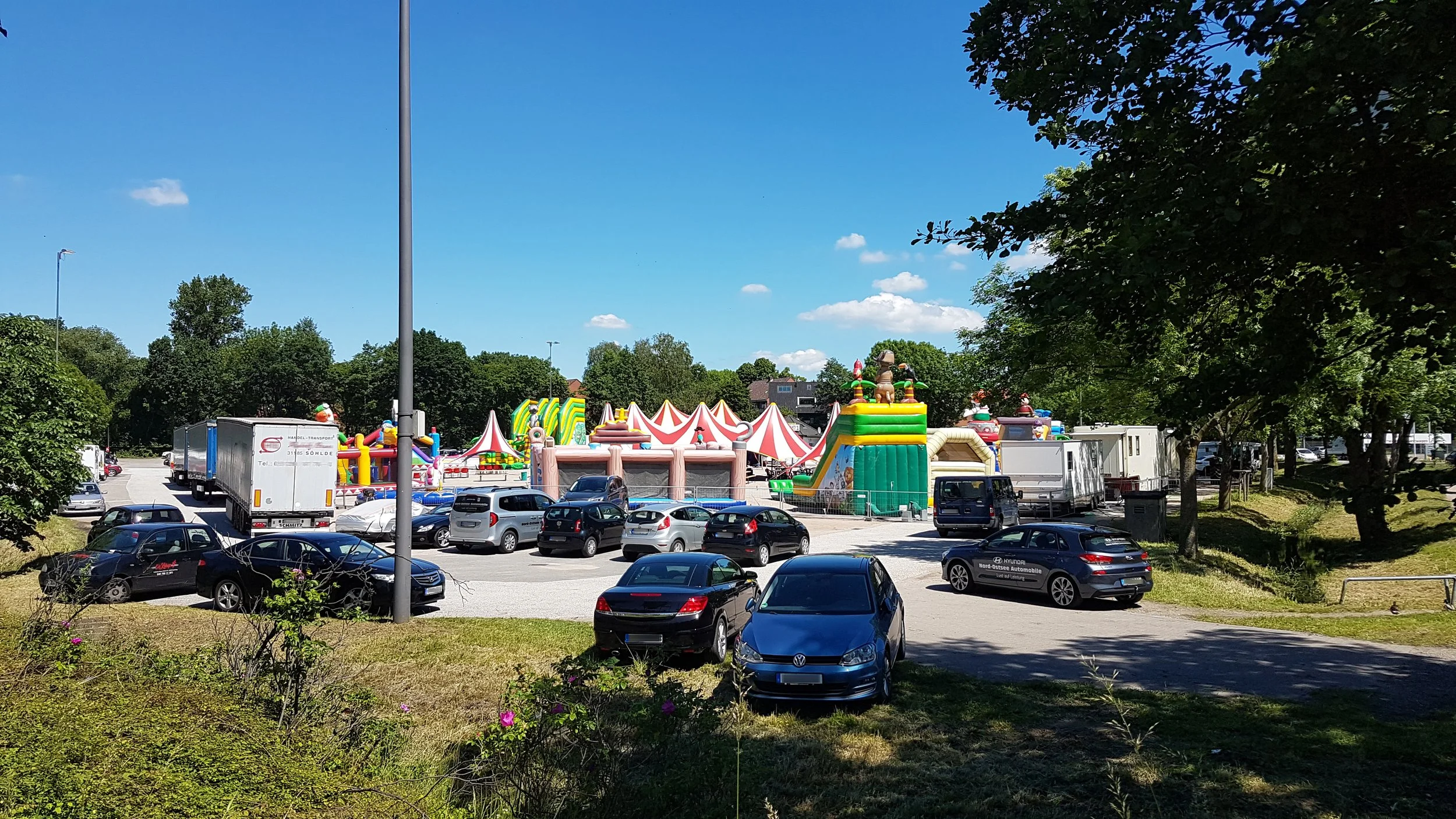 Frascatiplatz Hamburg Bergedorf. Vorne Autos und hinten bunte Hüpfburgen.