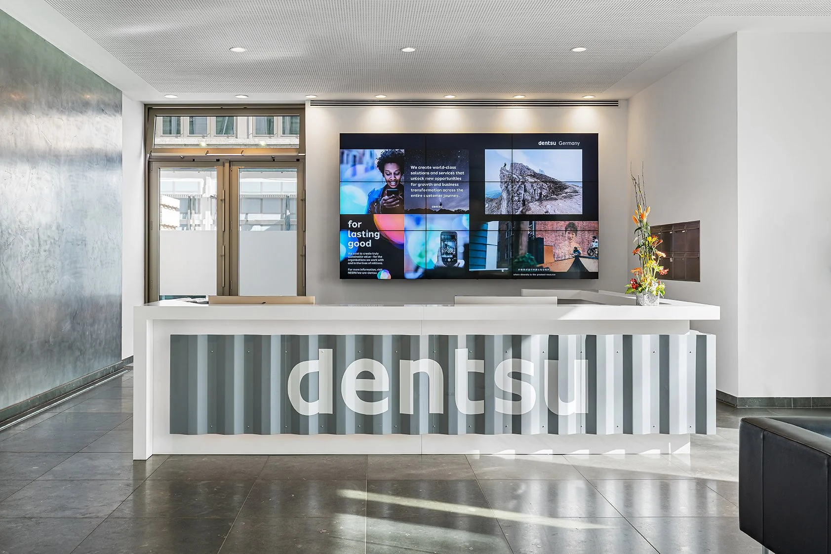 Dentsu Office: Blick auf eine Eingangsrezeption. Am Podest steht densu in weißen Buchstaben. Themenbereiche: Interior, Aufenthaltsqualität, Placemaking.