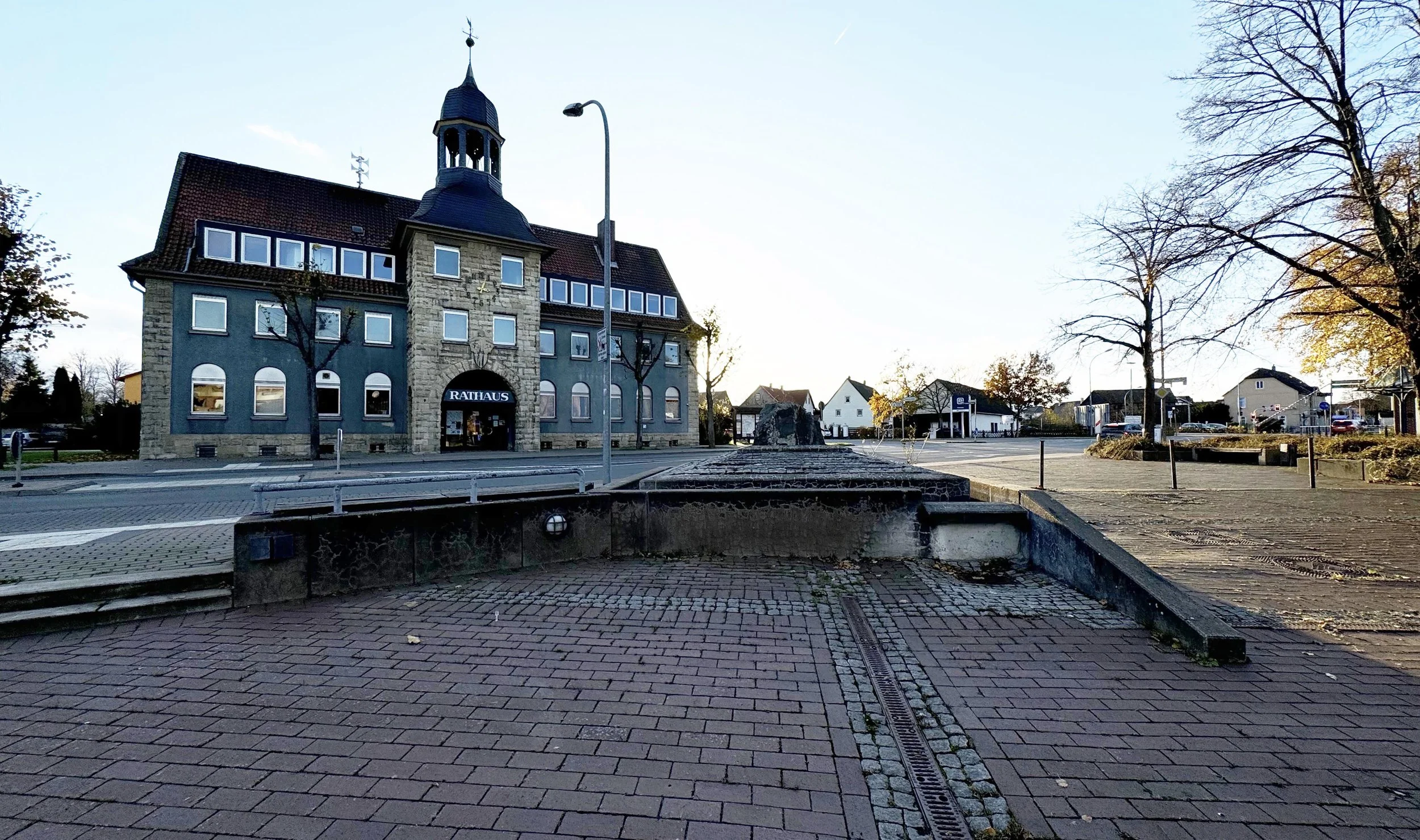 Foto Marktplatz Vienenburg. Vorne ein Brunnen ohne Wasser, dann eine Straße und dahinter das Rathaus von Vienenburg - ein historisches Gebäuzde mit einem Turm in der Mitte.