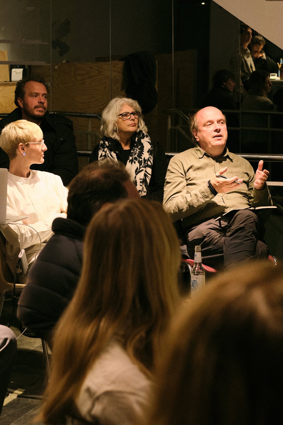 Mehrere Menschen sitzen in einem Raum während einer Diskussion oder Präsentation, einige nehmen Notizen oder hören aufmerksam zu.
