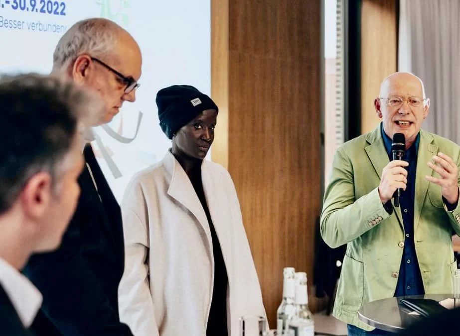 StadtTraum Bremen 2022. Der Bürgermeister Bovenschulte hält eine Rede mit Mikrofon bei einer Konferenz. Es sind weitere Personen im Raum, einige schauen aufmerksam zu, während er spricht. U.a. dabei Lars Zimmermann von CITIES FOR FUTURE