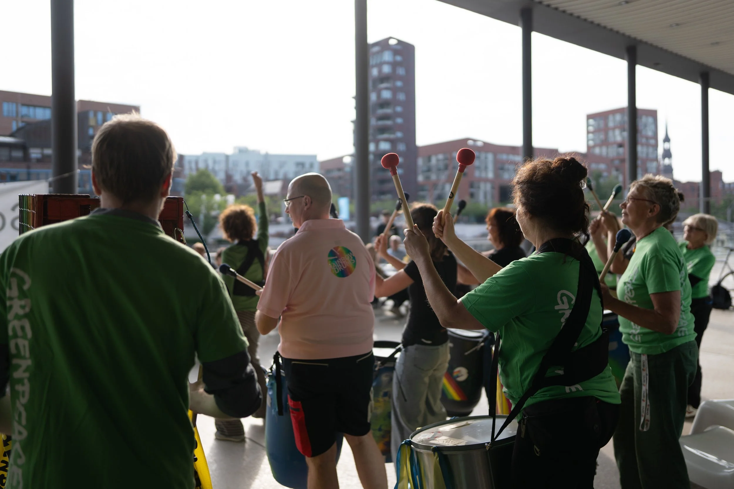 Menschen spielen Blasinstrumente in einer Gruppe im Freien, im Hintergrund eine Stadt mit modernen Gebäuden.