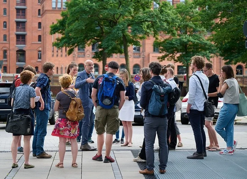 Ortsbegehung Projekt Altstadtküste Hamburg mit mehreren Personen draußen vor roten Speicherstadtgebäuden.