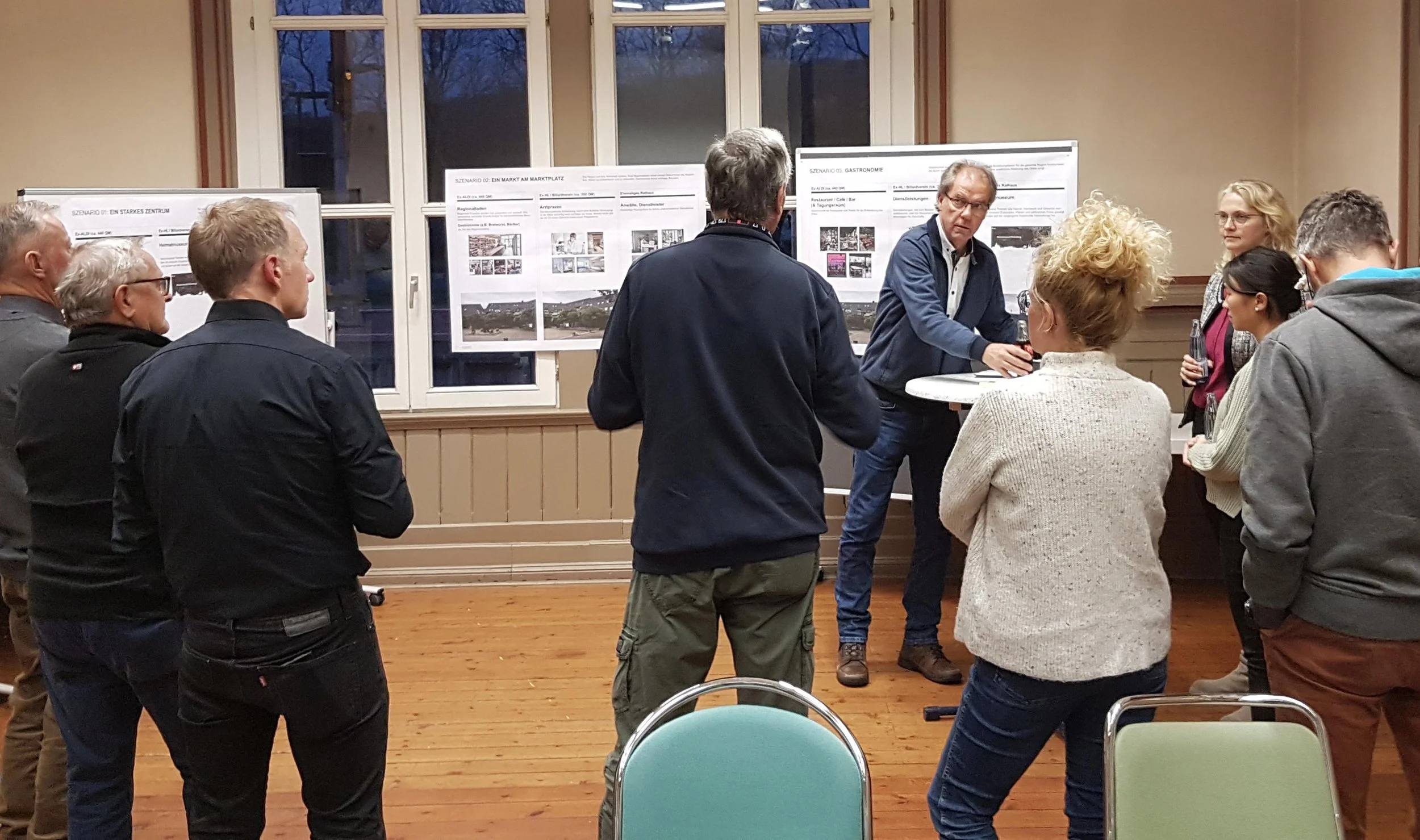 Foto vom Workshop für das Projekt Aufwertung Marktplatz Vienenburg. Mehrere Personen hören Klaus Mensing zu, der an den Whiteboards etwas erklärt.