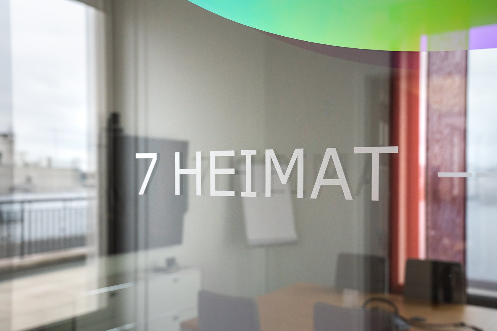 Dentsu Office: Glasscheibe mit Aufschrift 7 Heimat. Hintergrund unscharf. Ein Konferenzraum mit Stühlen und Tischen. Themenbereich: Interiorgestaltung, Innenarchitektur, Placemaking.