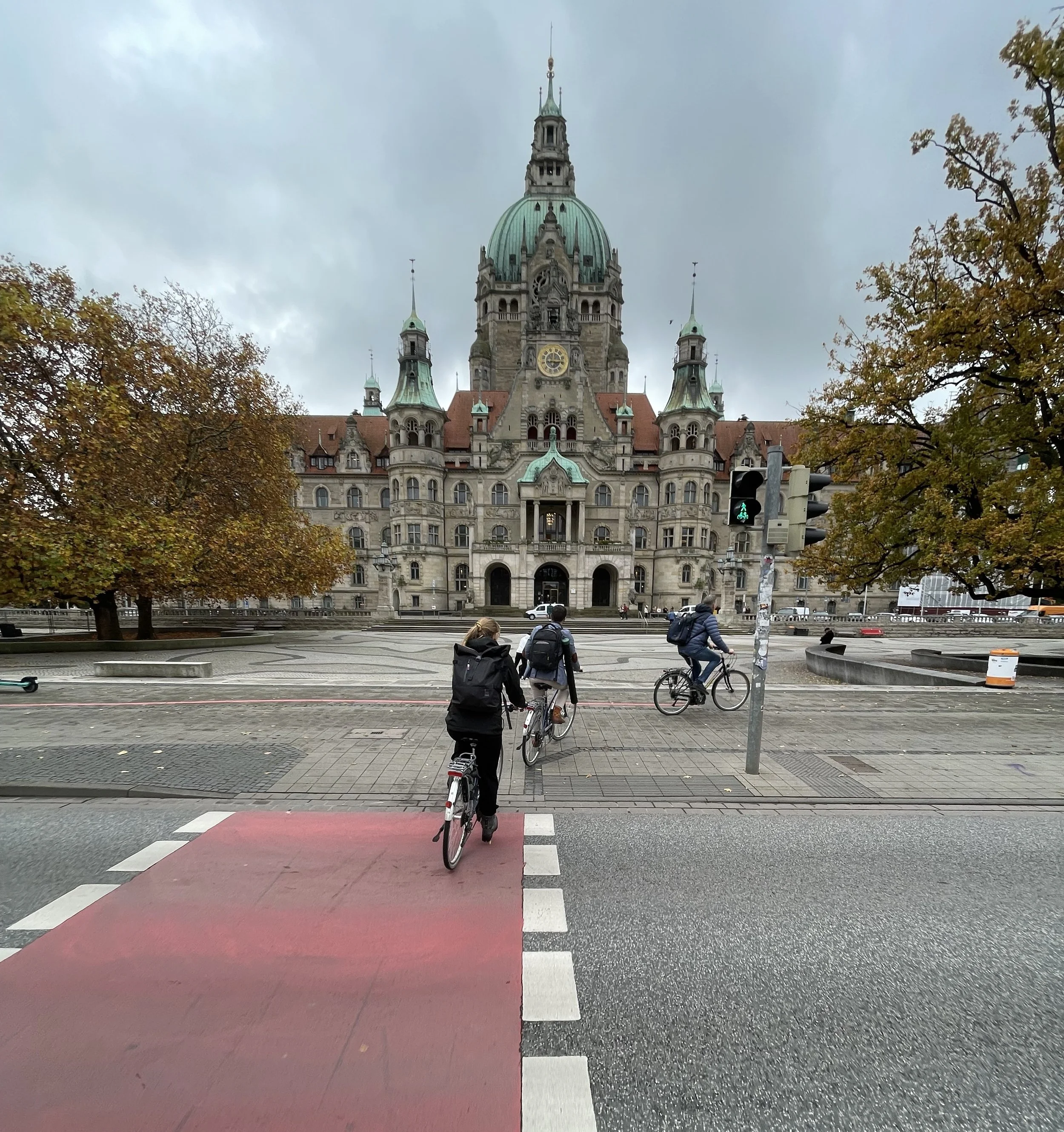 Foto mit Blick auf das Rathaus von Hannover. Im Vordergrund Straße und roter Radüberweg. Themenbereiche: Quartiersentwicklung, Aufenthaltsqualität, Mobilität.