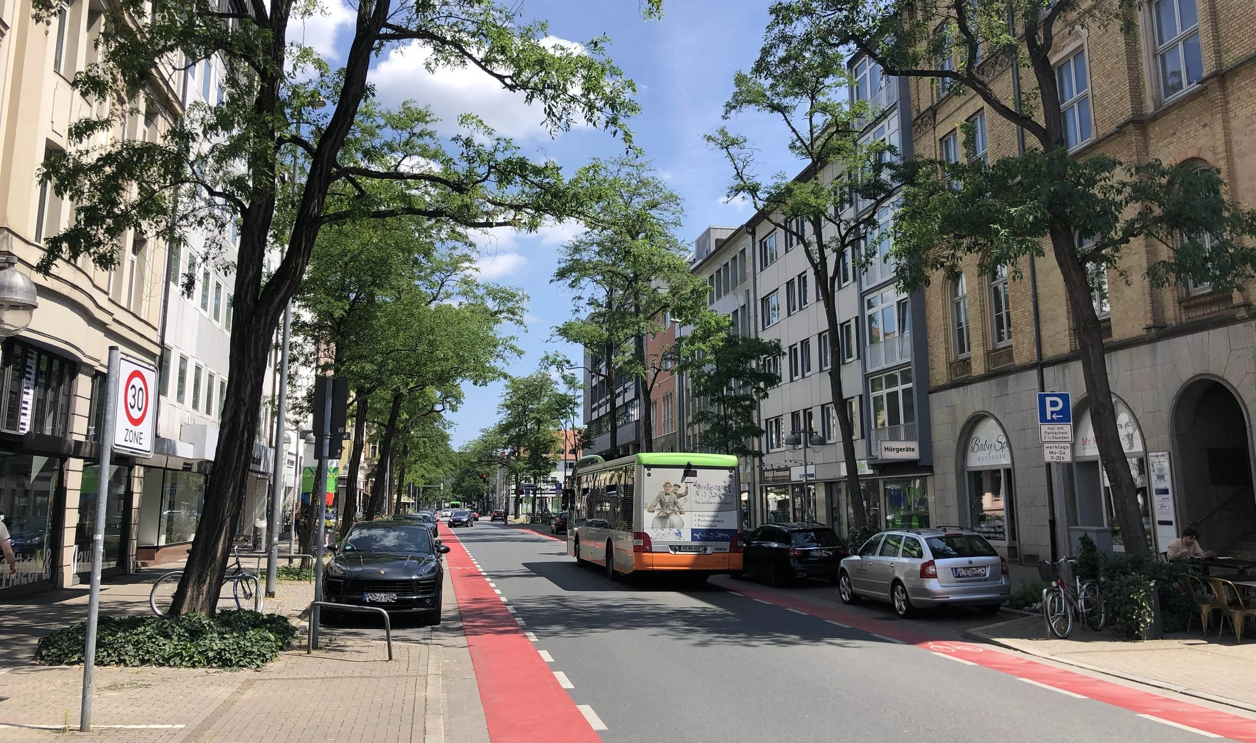 Foto einer Straße in Hannover mit roten Fahrradstreifen an den Rändern. Bäume und Gebäude an den Seiten.