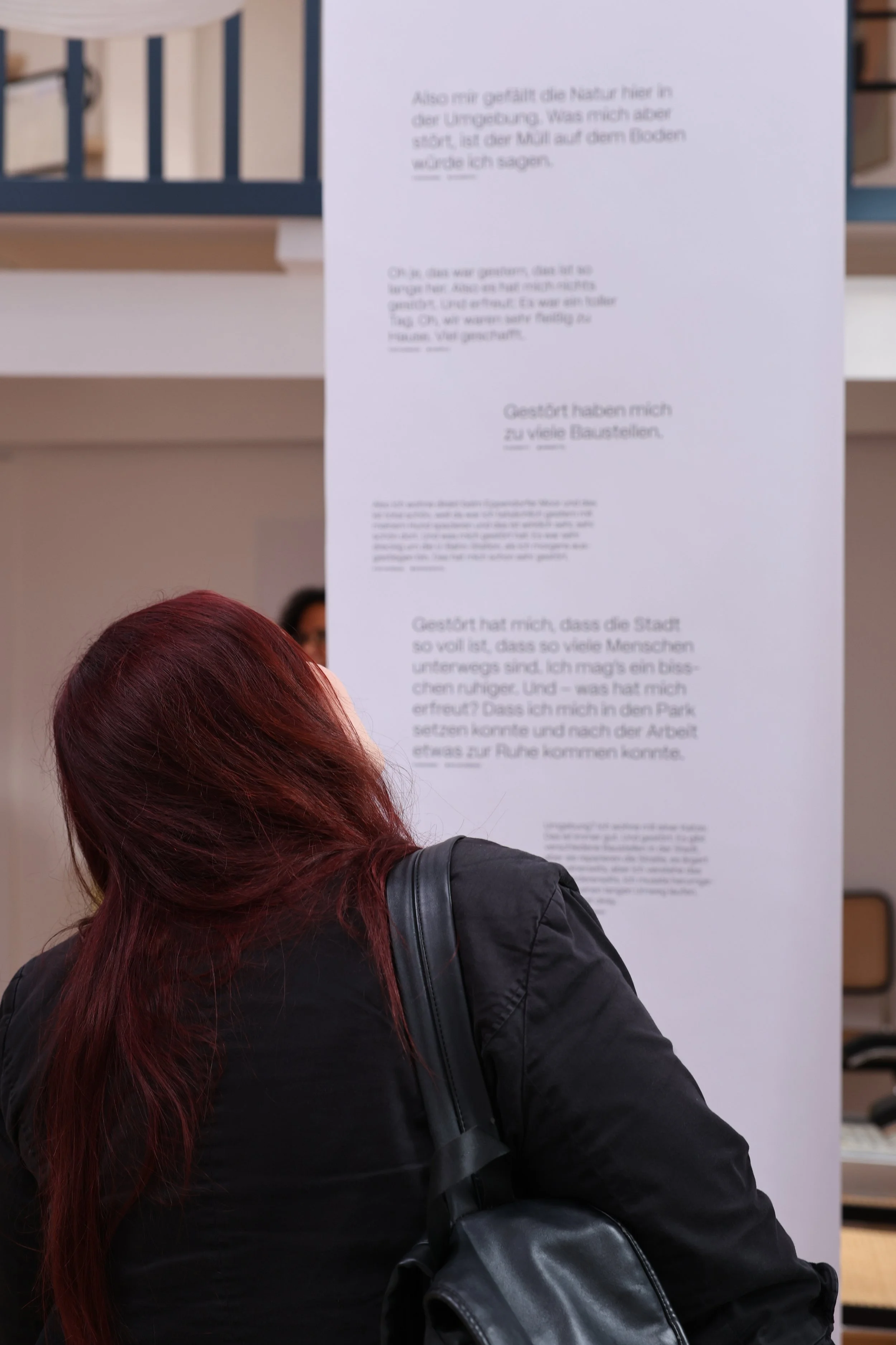Eine Person mit roten Haaren trägt eine schwarze Jacke und einen schwarzen Rucksack, steht vor einem Banner mit geschriebenen Texten zu Umfrageergebnissen auf Deutsch.
Hamburg Sustainability Week 2026. Ausstellung im Loft141.