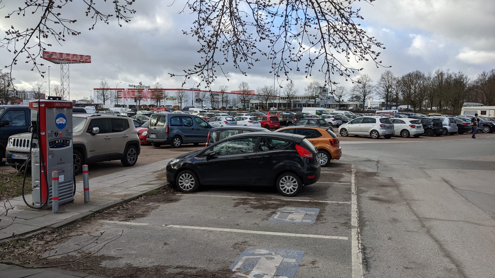 Frascatiplatz Hamburg Bergedorf. Links vorne Stellplätze mit Ladesäulen, hinten viele parkende Autos.