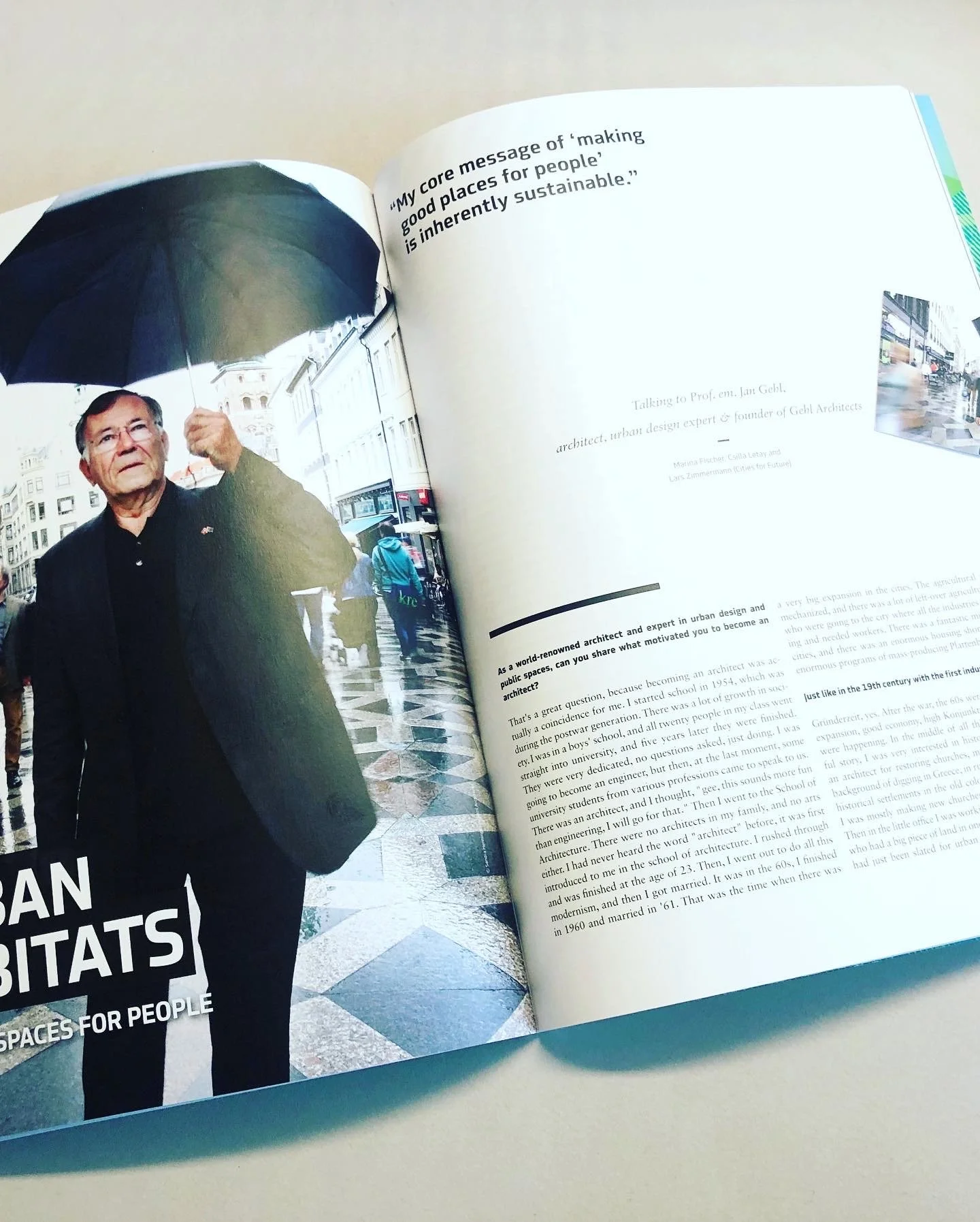 Jan Gehl hält in einer Fußgängerzone in der Hand ein schwarzes Regenschirm. Der Boden ist nass, Menschen gehen vorbei. Es ist bewölkt und regnet leicht.