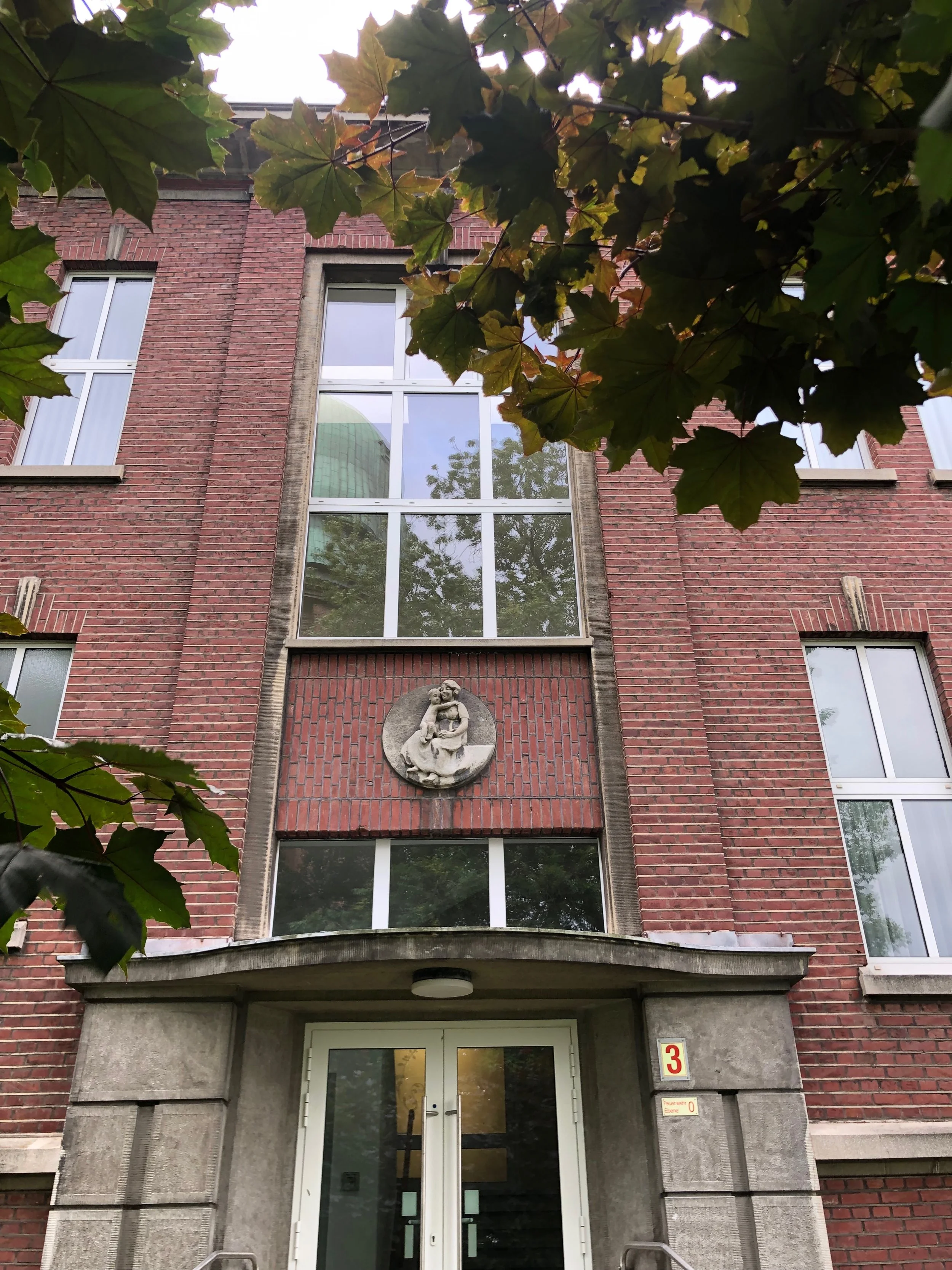 Foto des Eingangs vom Vialife Campus Bardenberg_Eingangsbereich von außen mit roten Backsteinen und grau mit Beton umrandeter Eingangstür.