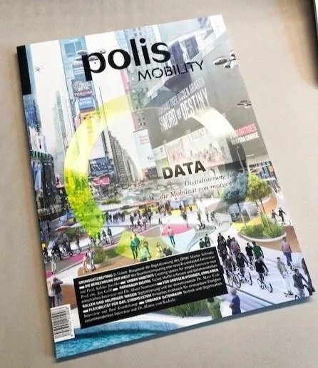 Zeitschrift mit dem Titel 'polis Mobility' liegt auf einem Tisch, mit einem Coverbild einer Stadtkreuzung mit Fußgängern, Fahrrädern und Autos, und enthält Texte über Stadtentwicklung, Design und Daten.