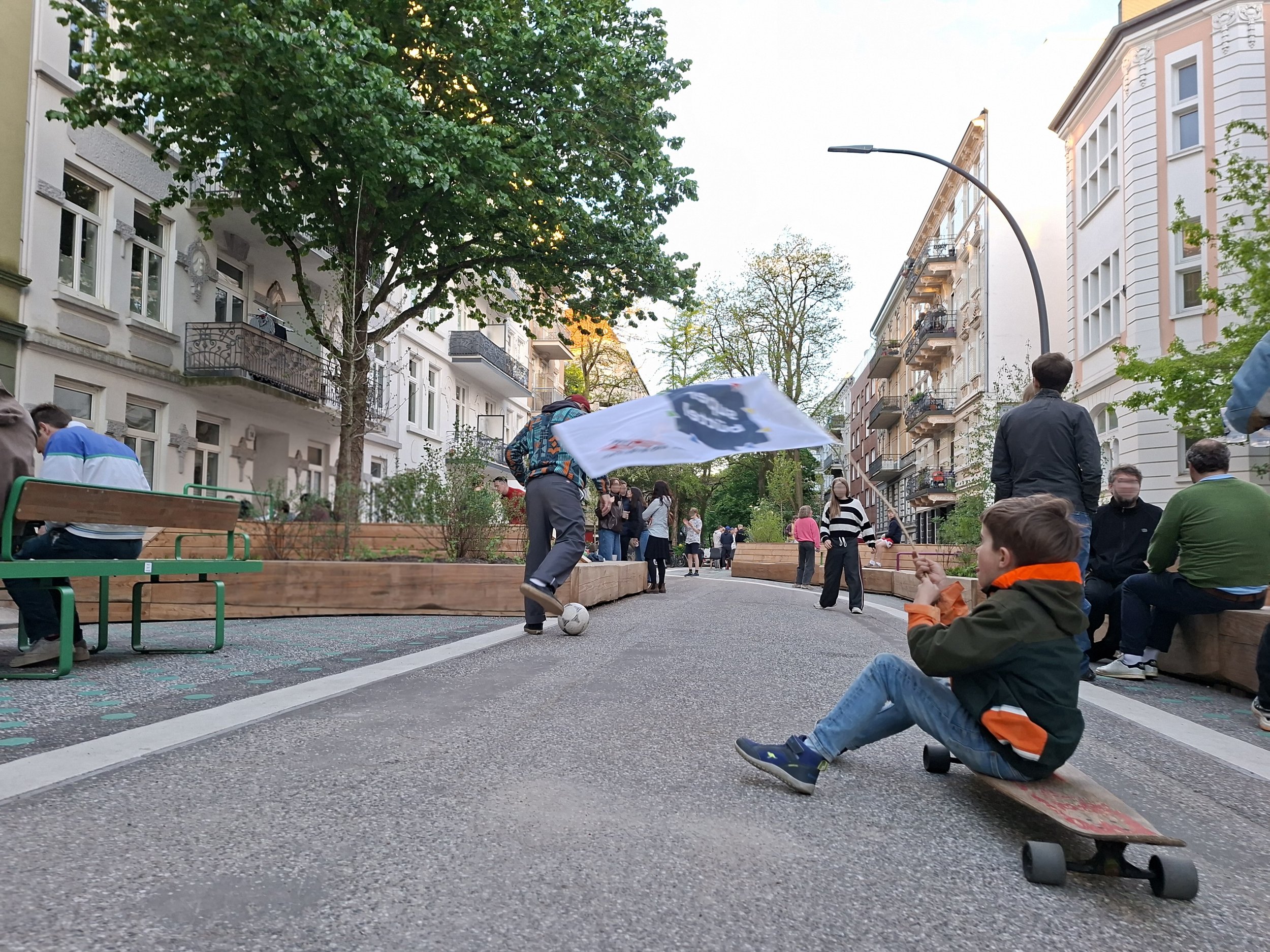 Schulstraße Rellinger Straße am 8. Mai 2026. Bänke, spielende Kinder, keine Autos.Themenbereiche: Superblocks, Aufenthaltsqualität, Mobilität.