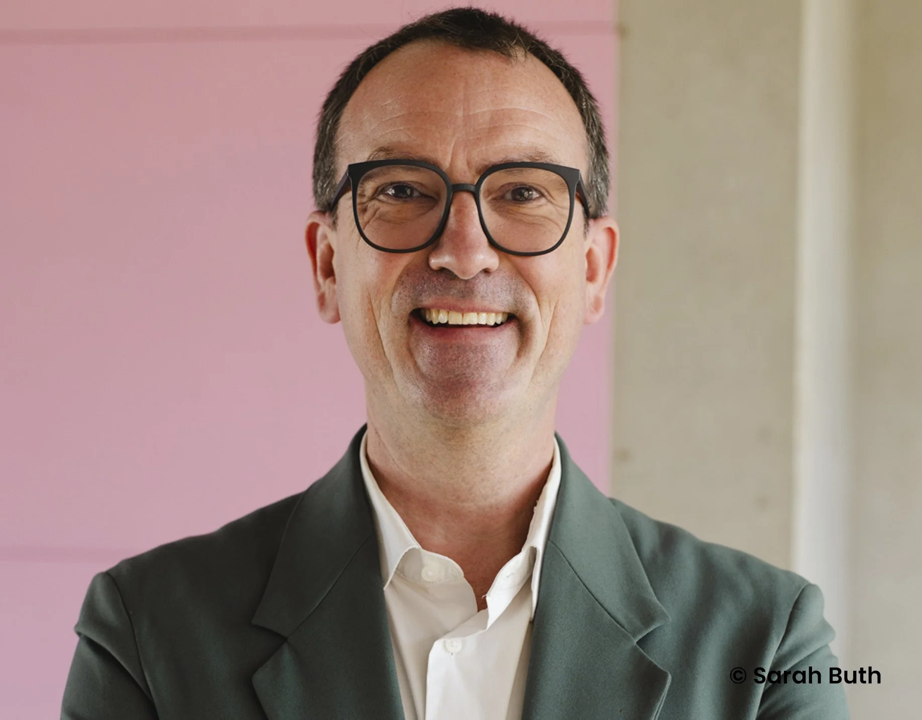 Lächelnder Mann mit Brille trägt Anzug vor buntem Hintergrund