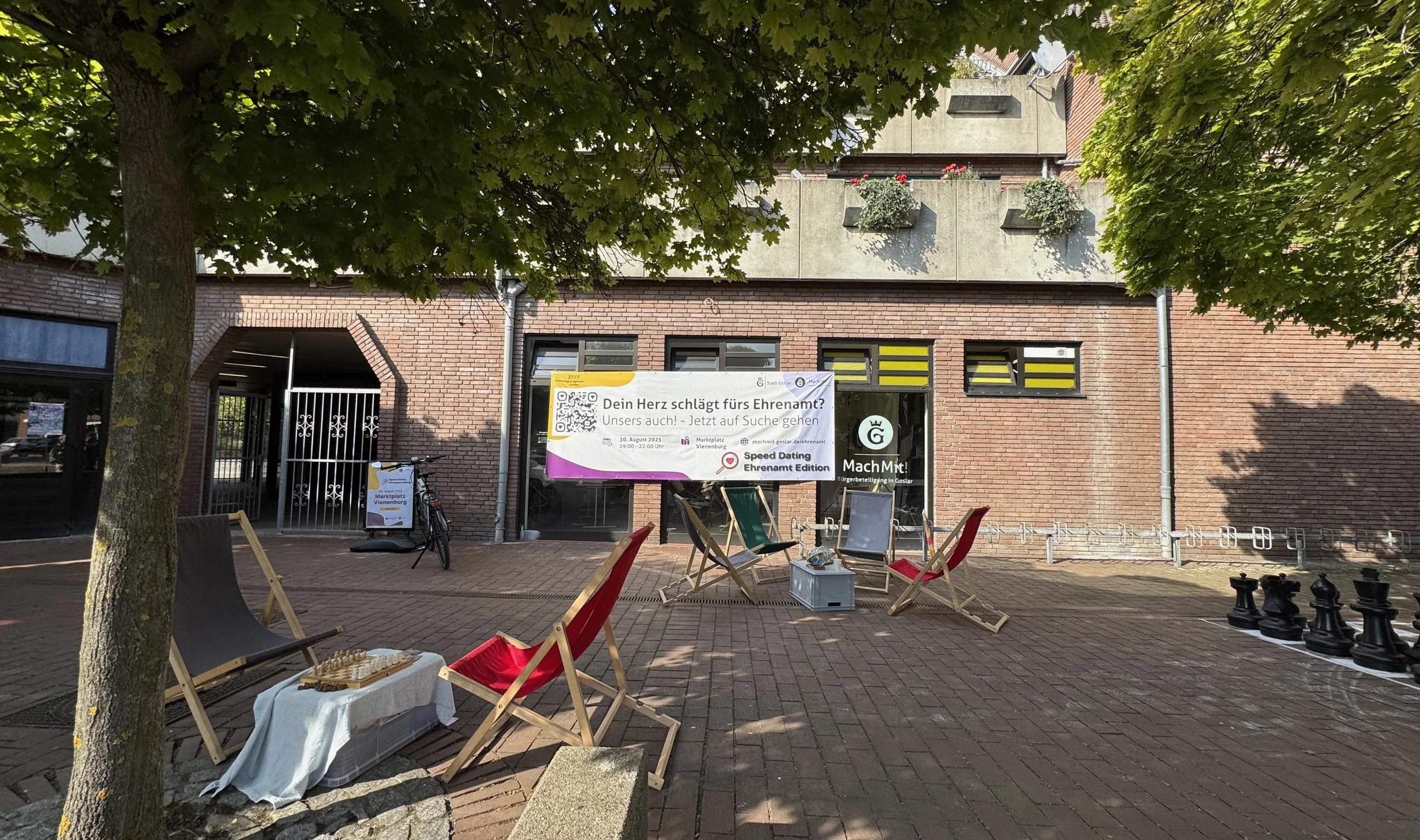 Marktplatz Vienenburg. Vorne und hinten Liegestühle in rot, daneben jeweils Tische und im Hintergrund ist eine Gebäudefassade mit einem Banner zu sehen.
