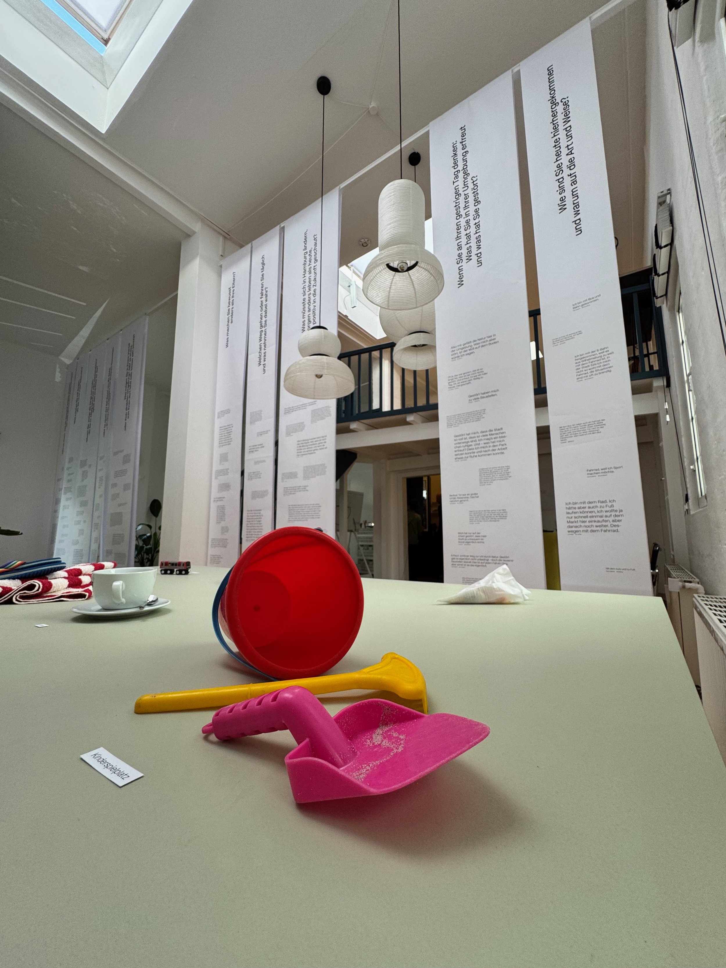 Ein Tisch mit buntem Spielzeug, darunter eine Schaufel. Im Hintergrund hängen weiße Papierbanner mit Text, und es gibt Lampen an der Decke.
Sustainability Week 2026. Ausstell