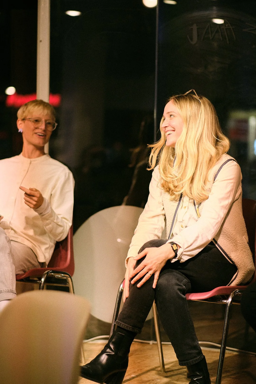 Zwei lachende Frauen sitzen in einem Raum und unterhalten sich.