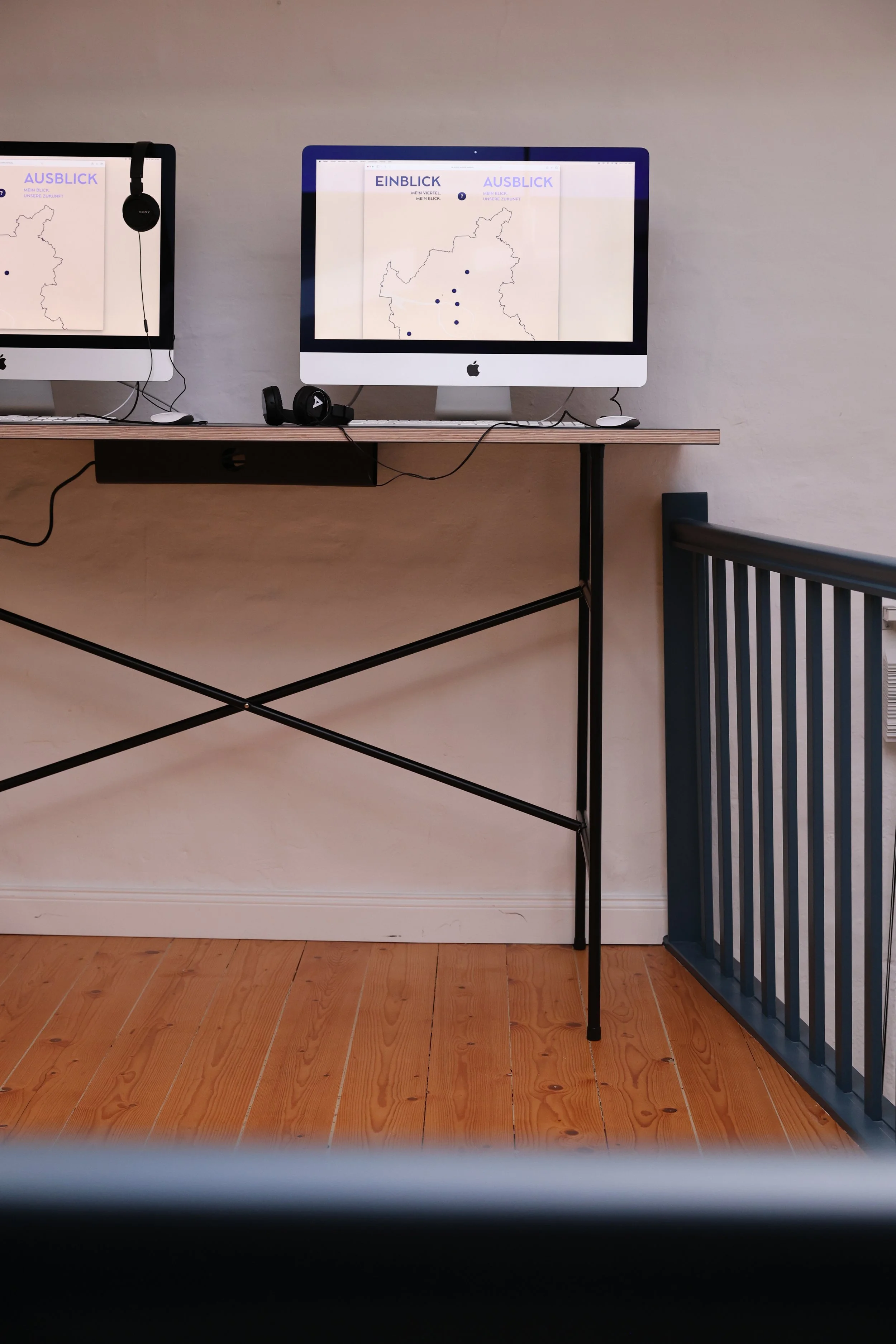 Zwei iMac-Computer auf einem Tisch, beide Bildschirme zeigen eine Karte mit der Aufschrift 'EINBLICKE' und 'AUSBLICKE'. Es gibt Kopfhörer an den Computern, Kabel hängen herunter.
Sustainability Week 2026. Ausstellung im Loft141.