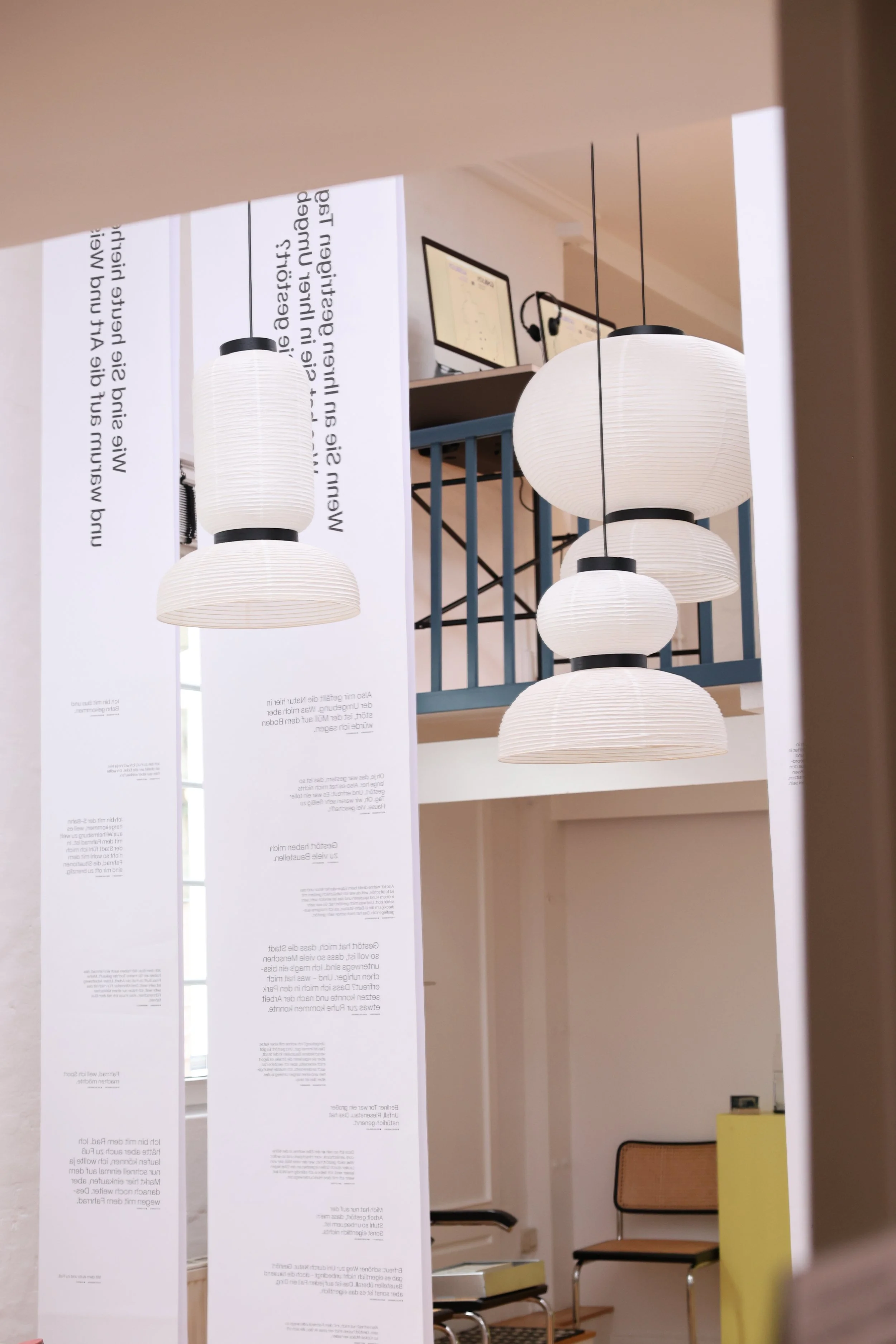 Der Blick neben den Banner von der Decke zeigt eine weiße Raumdecke mit mehreren weißen Papierlaternenlampen, einen blauen Büroregal mit Monitoren und einen Stuhl im Hintergrund.
Hamburg Sustainability Week 2026. Ausstellung im Loft141.