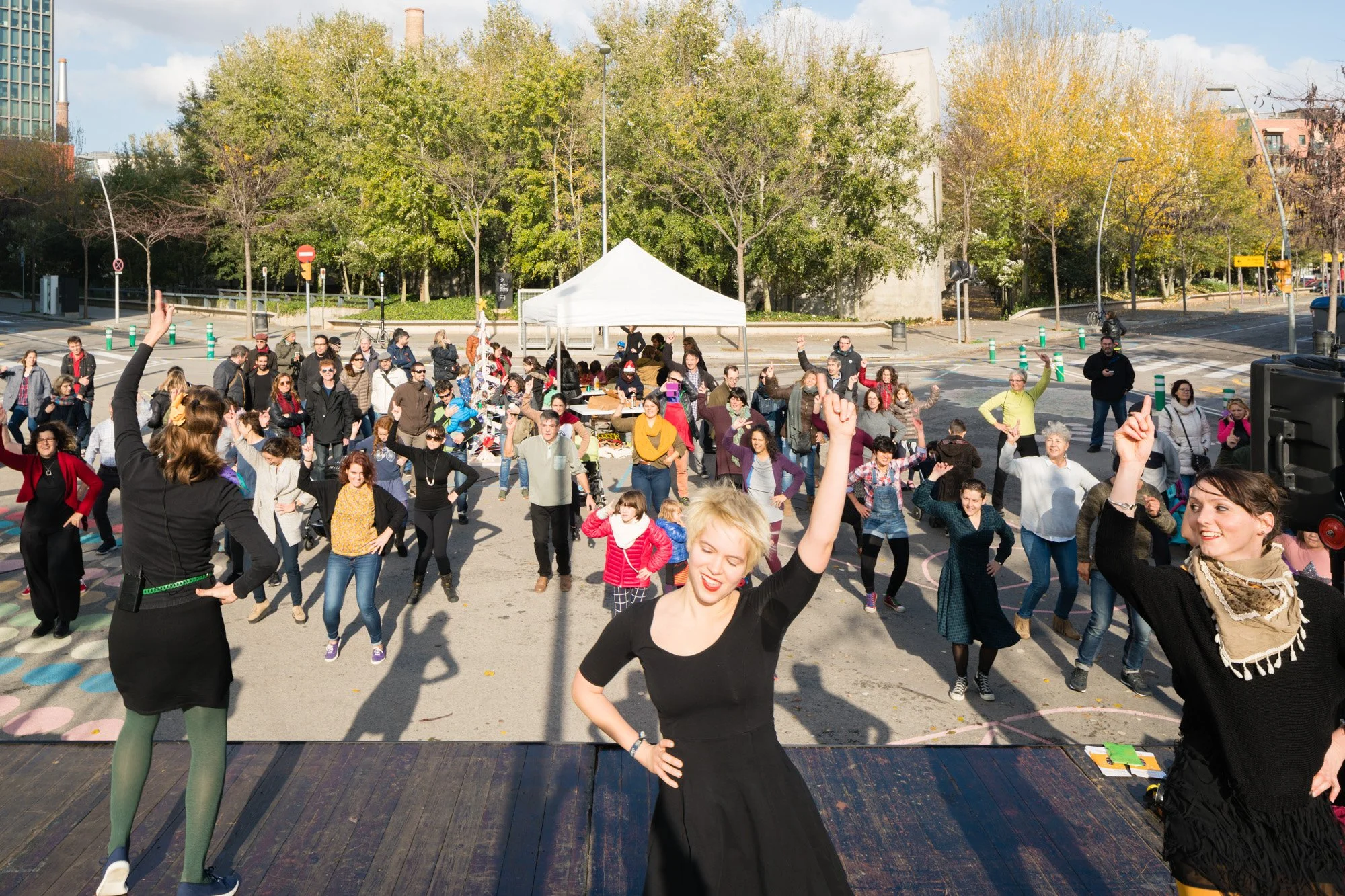 Menschen bei einer Outdoor-Veranstaltung, tanzen und feiern vor einer weiße Zelt, mit Bäumen im Hintergrund.