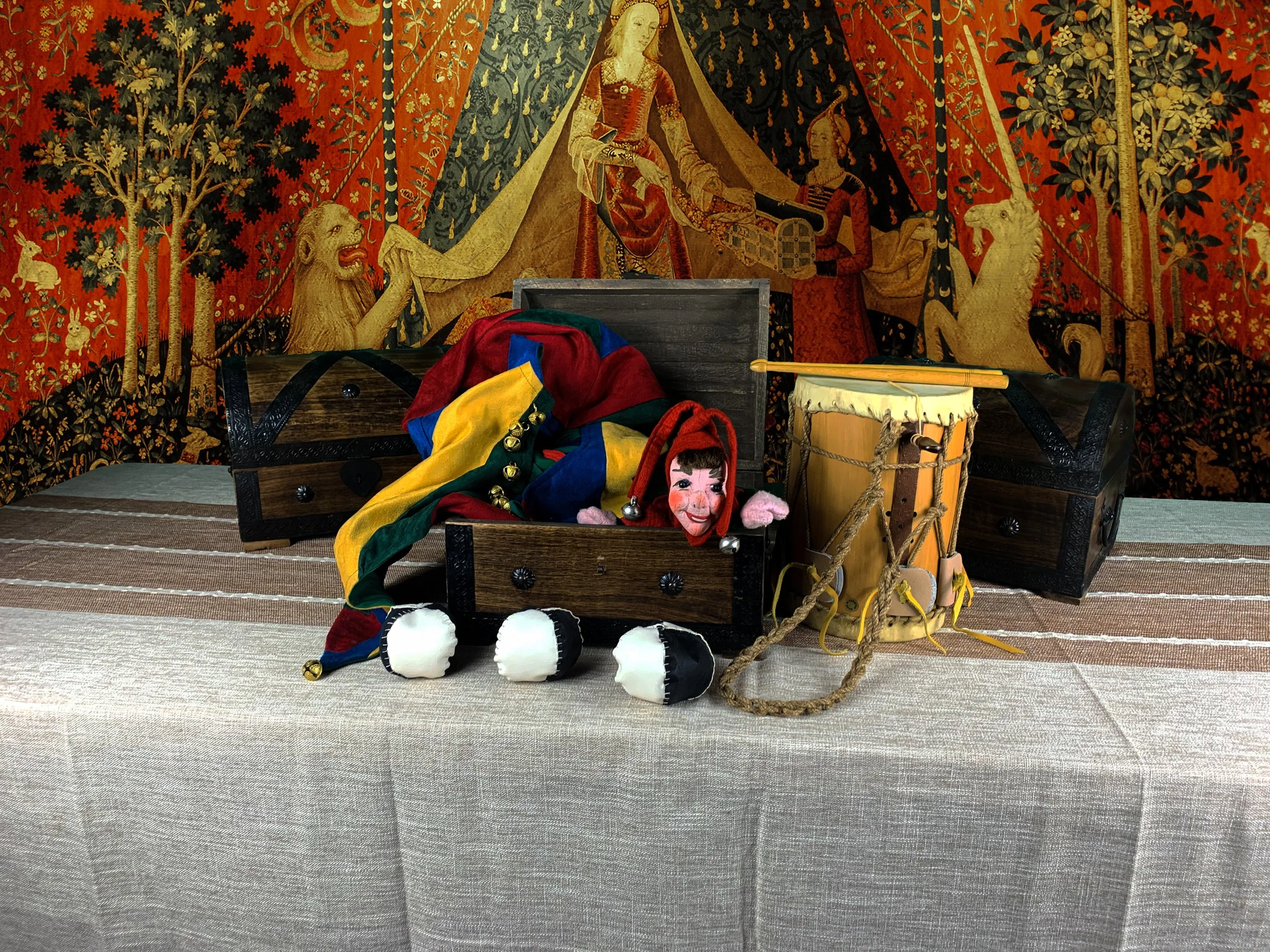 Display of puppets and costumes on a table with a medieval tapestry background.